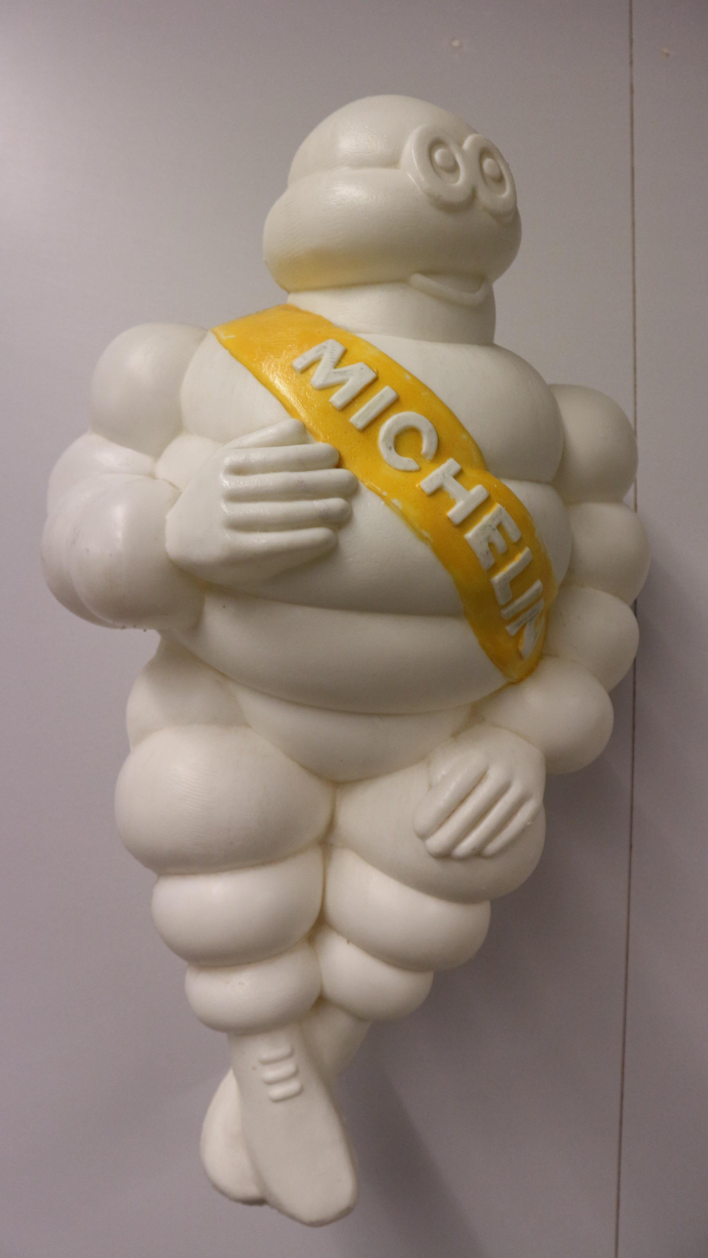 vintage white Bibendum Michelin advertising sign from plastic 1960s France. The Michelin man was made of white plastic and shows a yellow ribbon across its body with the white emblem Michelin.
The Bibendum Michelin was the mascot for many