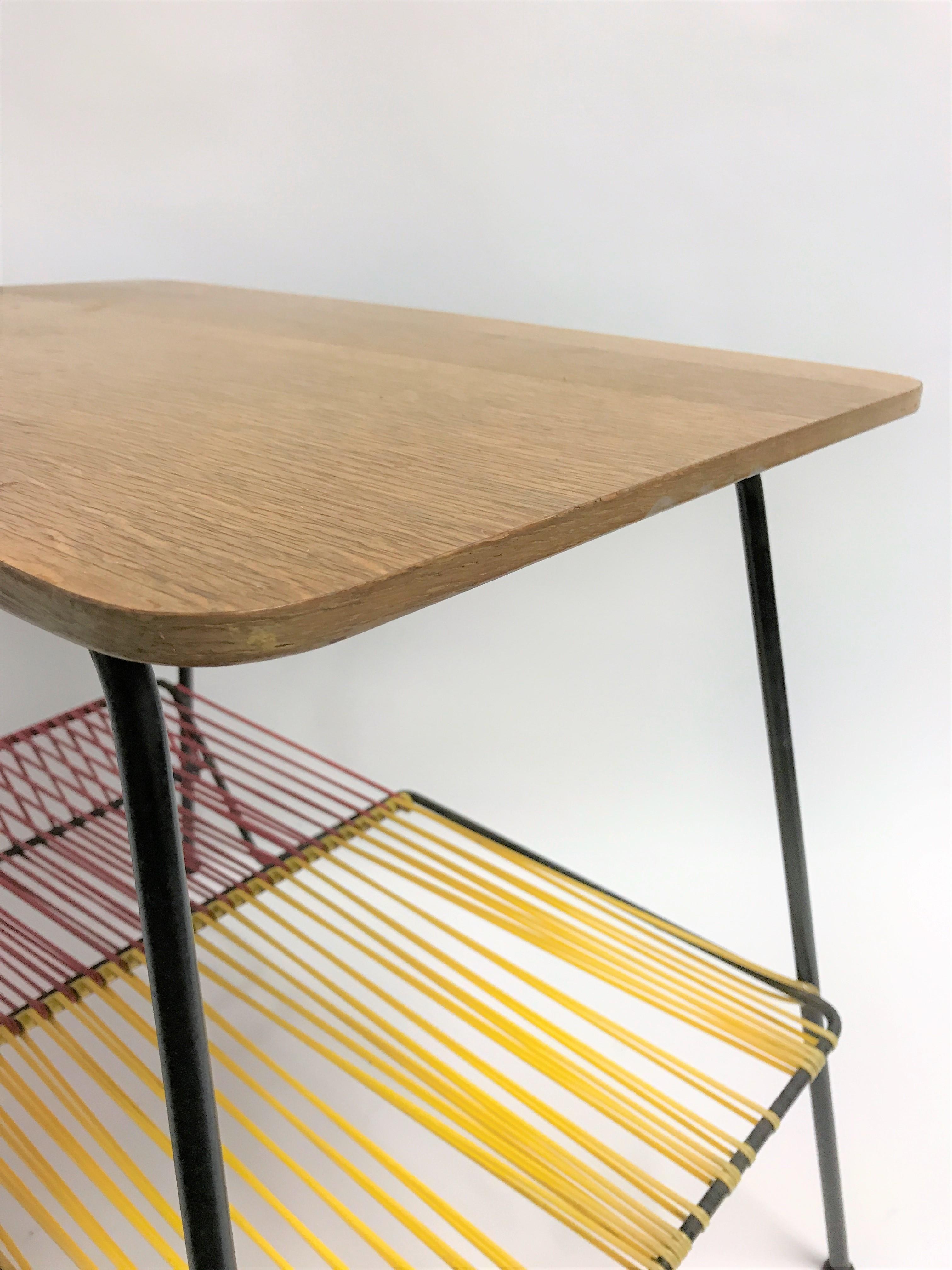 Midcentury plastic cord or 'scoubidou' side table.

Black metal frame with a plastic cord magazine 'shelve' and a wooden top

Very colorful and decorative midcentury piece.

1950s - France

Measures: Height 58cm/22.83
