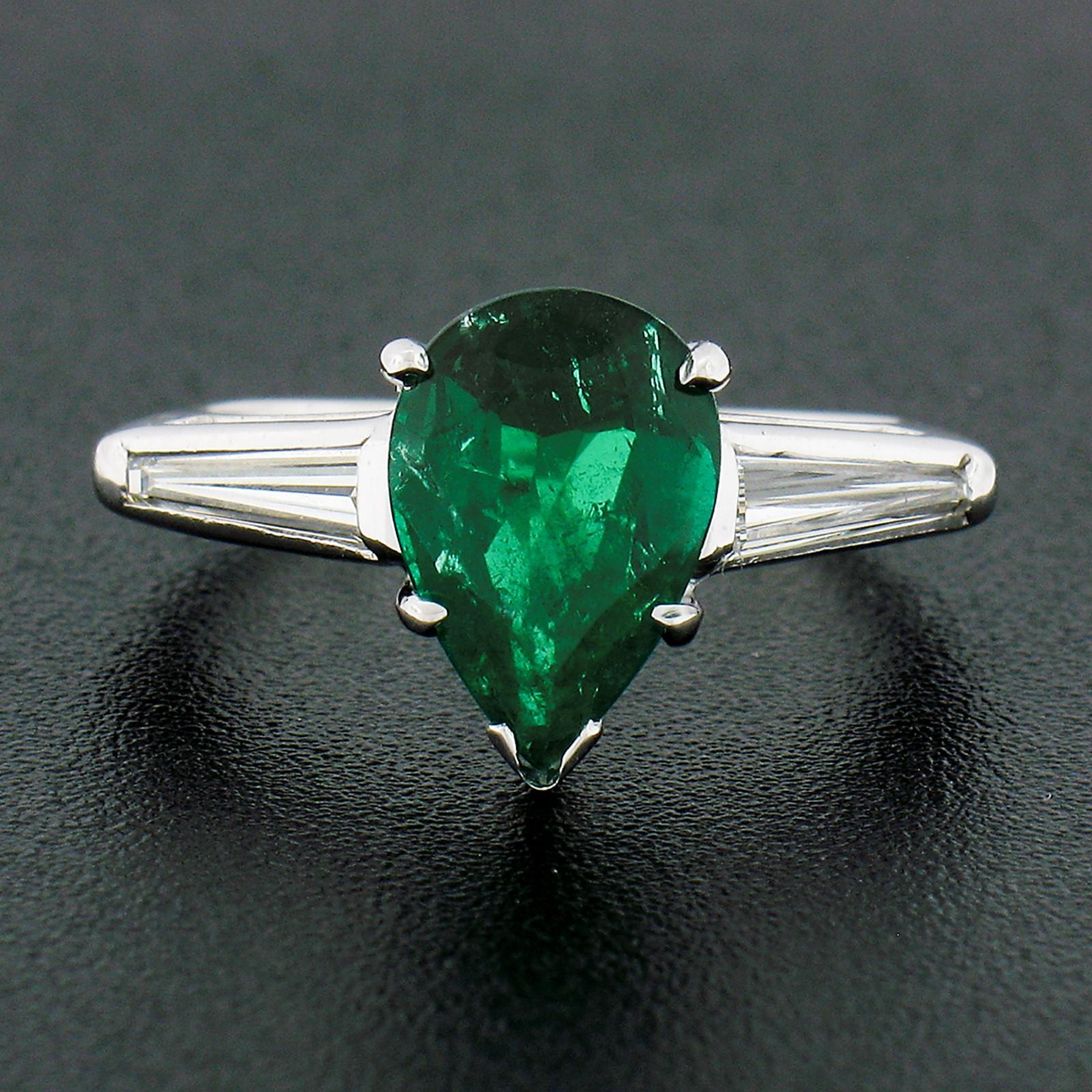 This stunning vintage ring is crafted from solid platinum and features an, SSEF certified, natural emerald and diamond three-stone design. The breathtaking pear cut emerald displays the finest and most desirable rich and deep green color and is very
