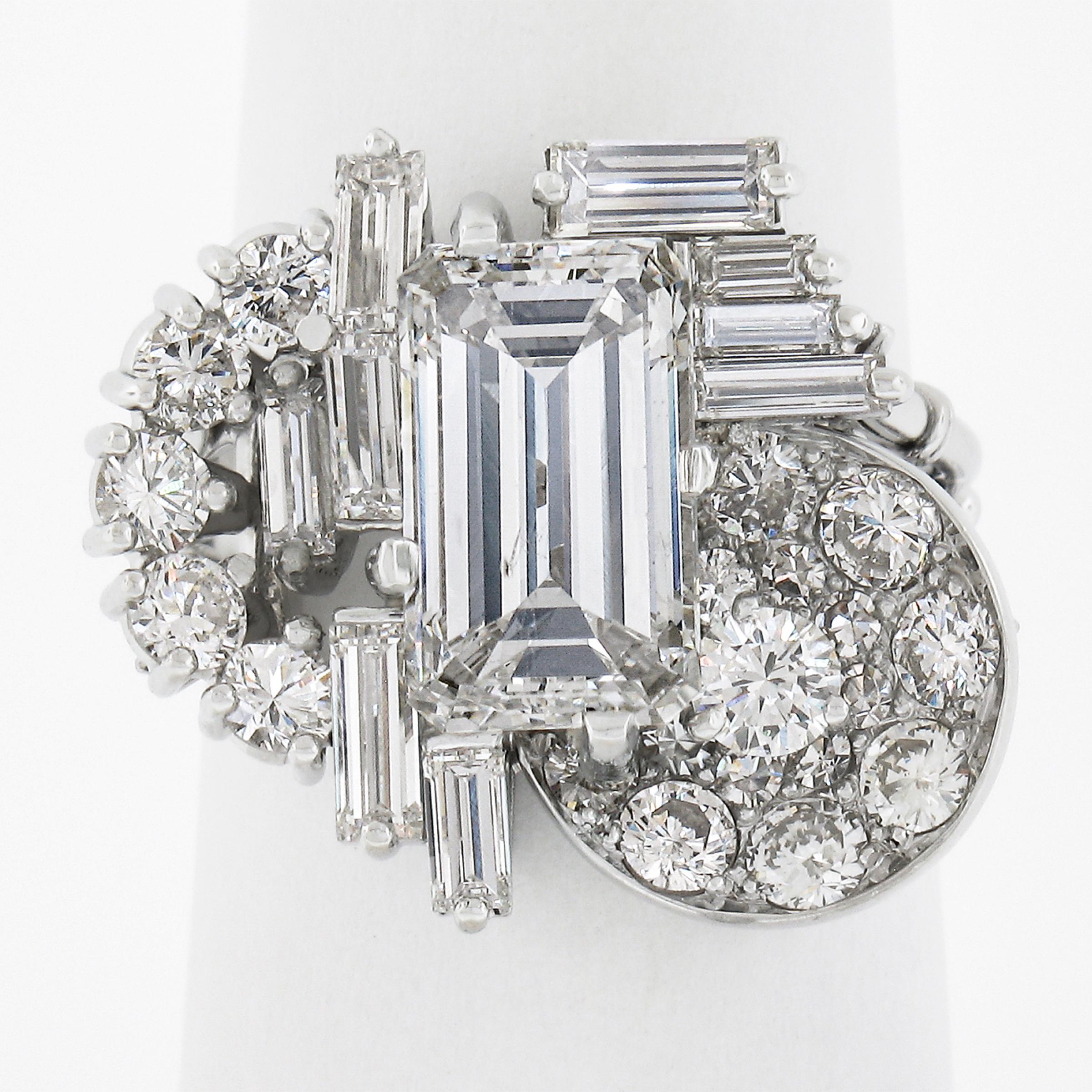 This super glamourous and fancy diamond statement ring is crafted in solid platinum and features a large, 3.0 carat emerald cut diamond at the center of the design. It is uniquely surrounded by baguette and round cut diamonds that total