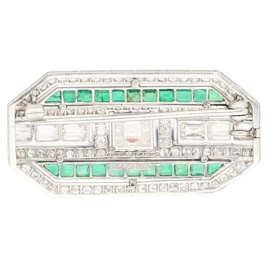 Art Deco pendant/brooch featuring a rectangular step-cut diamond of approx. 1.65 carats, accented by full and single-cut diamonds weighing a total of approximately 2.00 carats. Flanked by calibré-cut synthetic emeralds, set in platinum, signed Bert