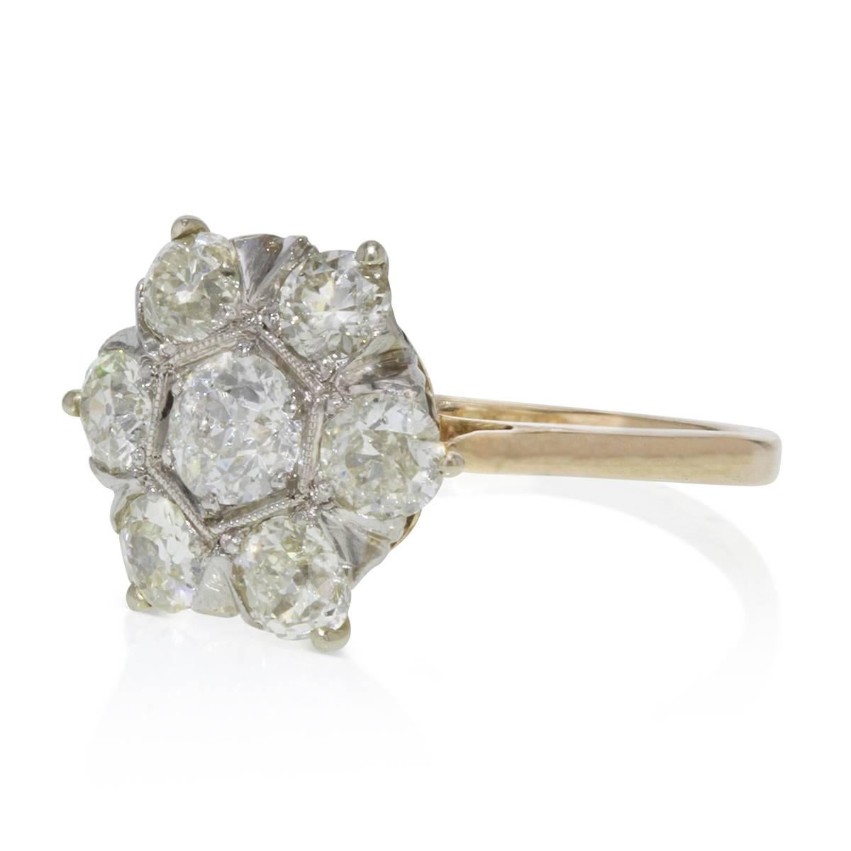 This relatively petite cluster or flower ring works beautifully as a somewhat unconventional engagement ring. Seven bright-white old minor sparklers, set in platinum adorned by milgrain edging on a yellow gold shank, join forces to create this