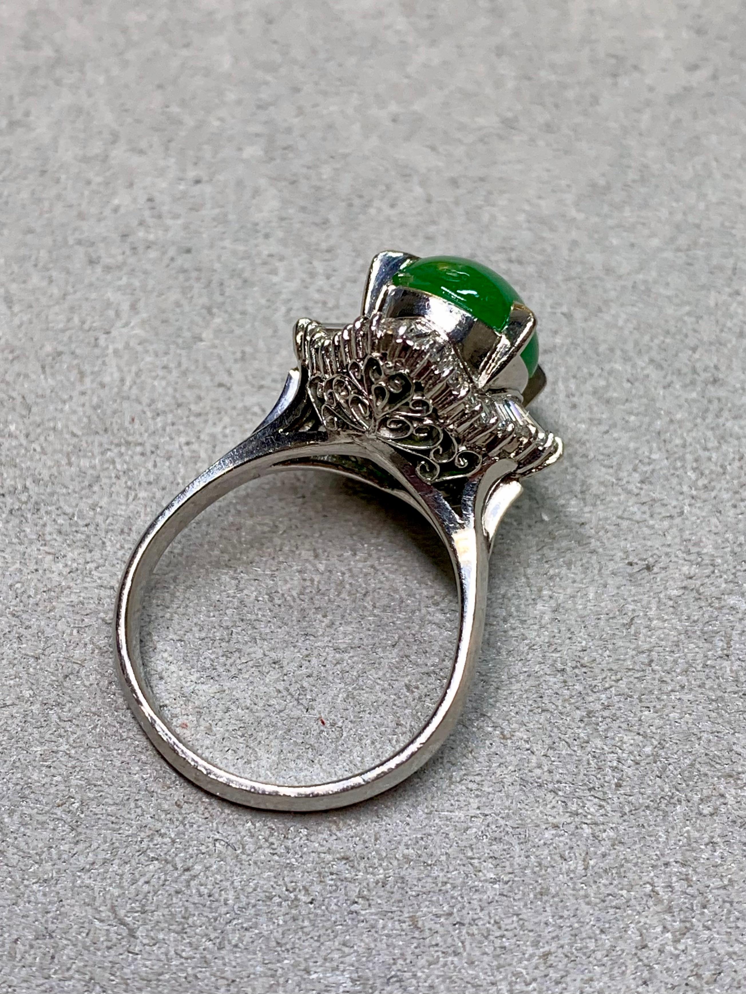 A vintage platinum ring centered by a cabochon jade weighing approximately 7.22 carats. Surrounding the jade is a radiant halo of tapered baguette diamonds, creating an elegant and balanced design. The ring is finished with a detailed under gallery,