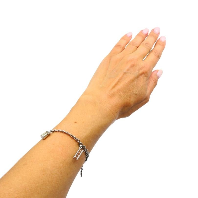 Esta pulsera vintage está elaborada en platino y diseñada con una serie de colgantes. Cada amuleto tiene una forma y un tema distintos. Entre ellas hay una escalera, un cubo, la figura de un soldado, una persona con una flor y un disco engastado con
