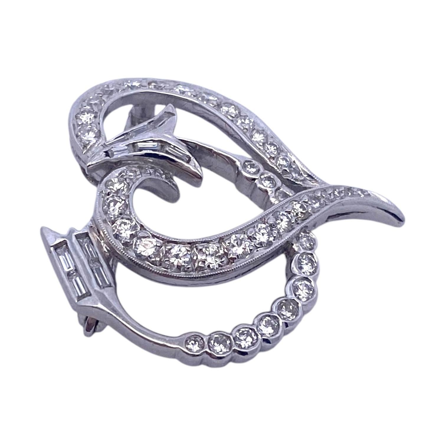 Vintage platinum brooch featuring a stylish diamond set heart and arrow design. The piece showcases a graceful arrangement of round brilliant and baguette cut white diamonds, accentuating its unique style. The brooch can also be worn as a pendant,