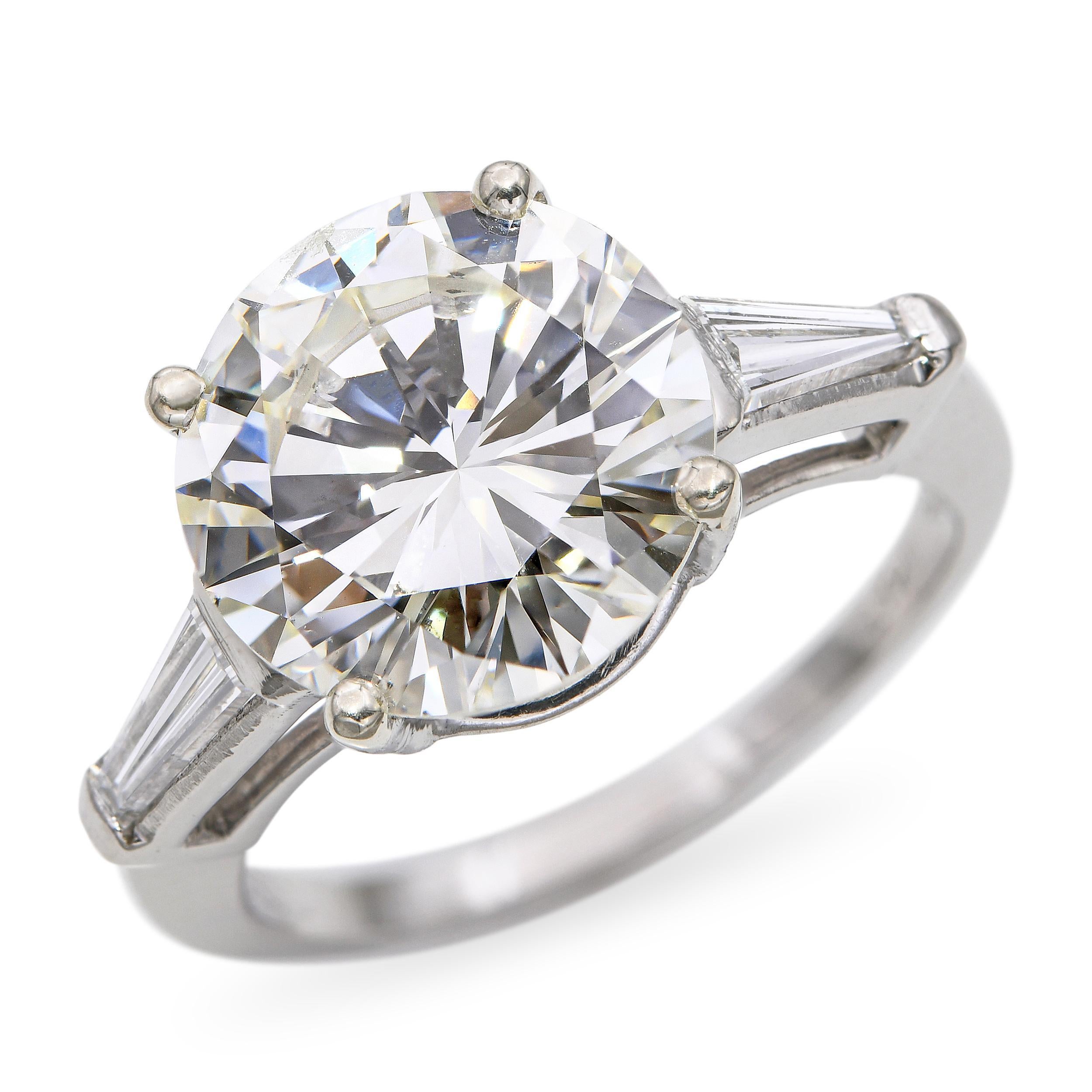 Cette bague vintage en platine est ornée d'un important diamant central de 3,84 carats certifié par la GIA, de pureté SI1 et de couleur M, ce qui lui confère une présence chaleureuse et antique. La pierre centrale est complétée par d'autres diamants