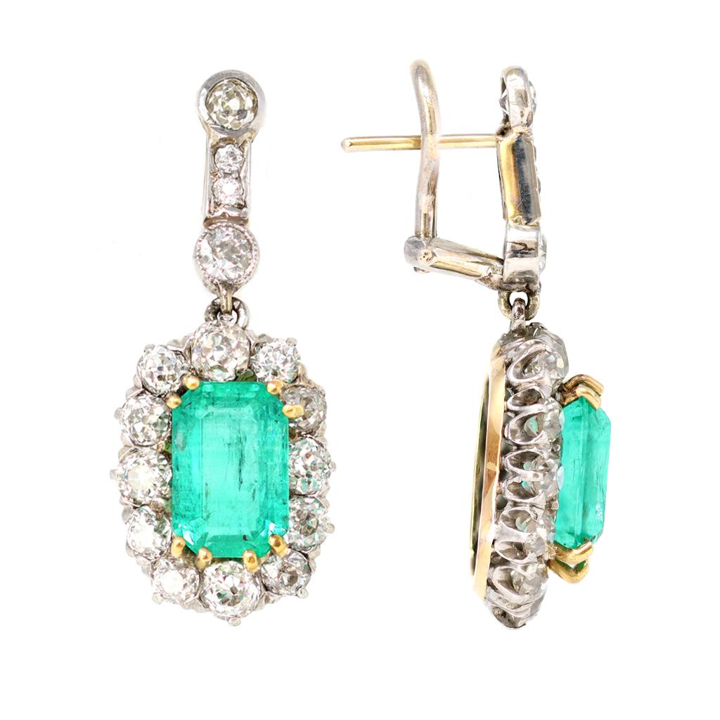 The vintage dangling clip-on earrings are composed of step cut faceted Colombian emeralds in the center of a halo of old mine cut diamonds. The well saturated rectangular shape emeralds have an estimated weight of 2.05 carats each. The old mine cut