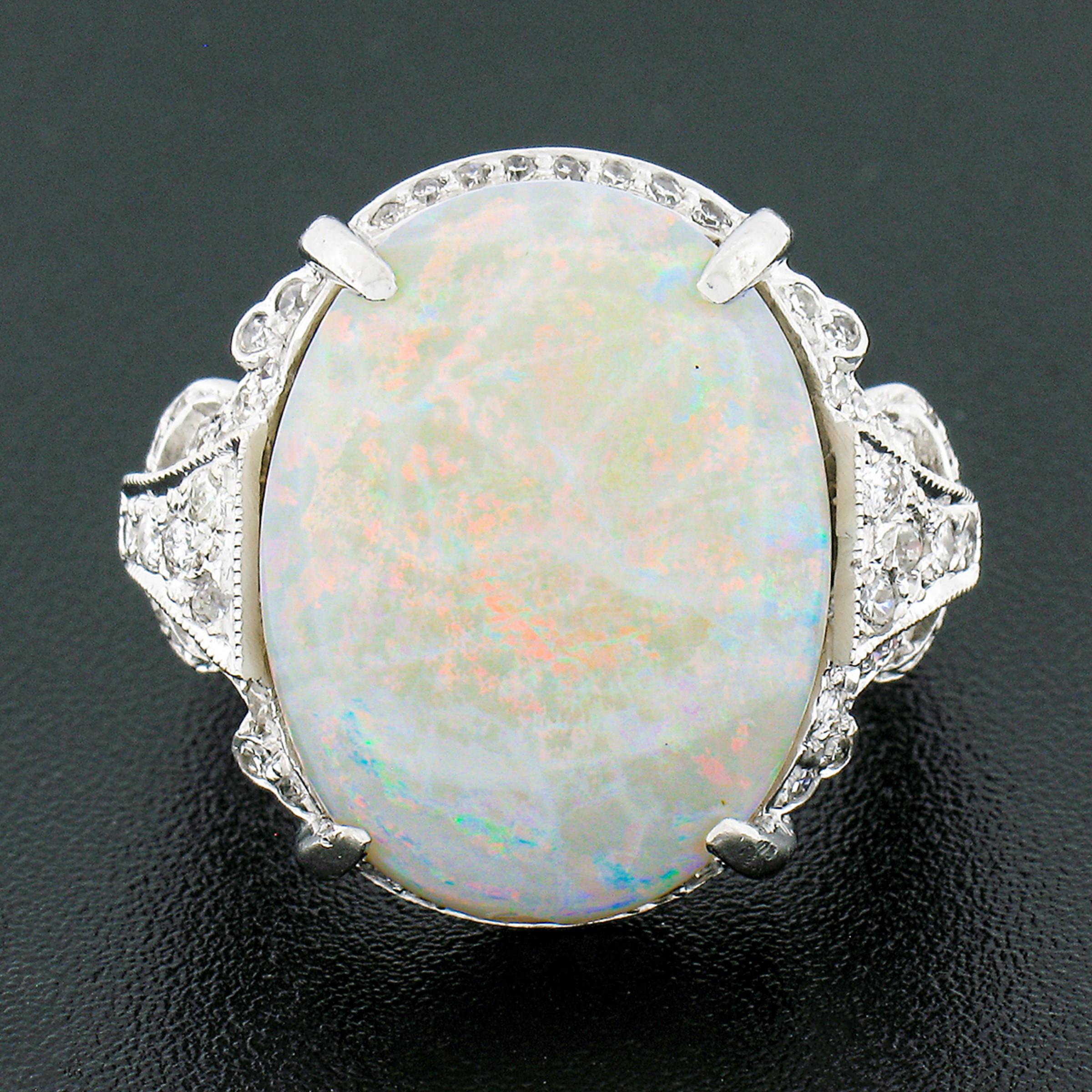 This stunning opal and diamond vintage cocktail ring is crafted in solid platinum and features an outstanding oval cabochon cut opal stone neatly prong set on an open basket at the center. This large stone has a beautiful white base color showing