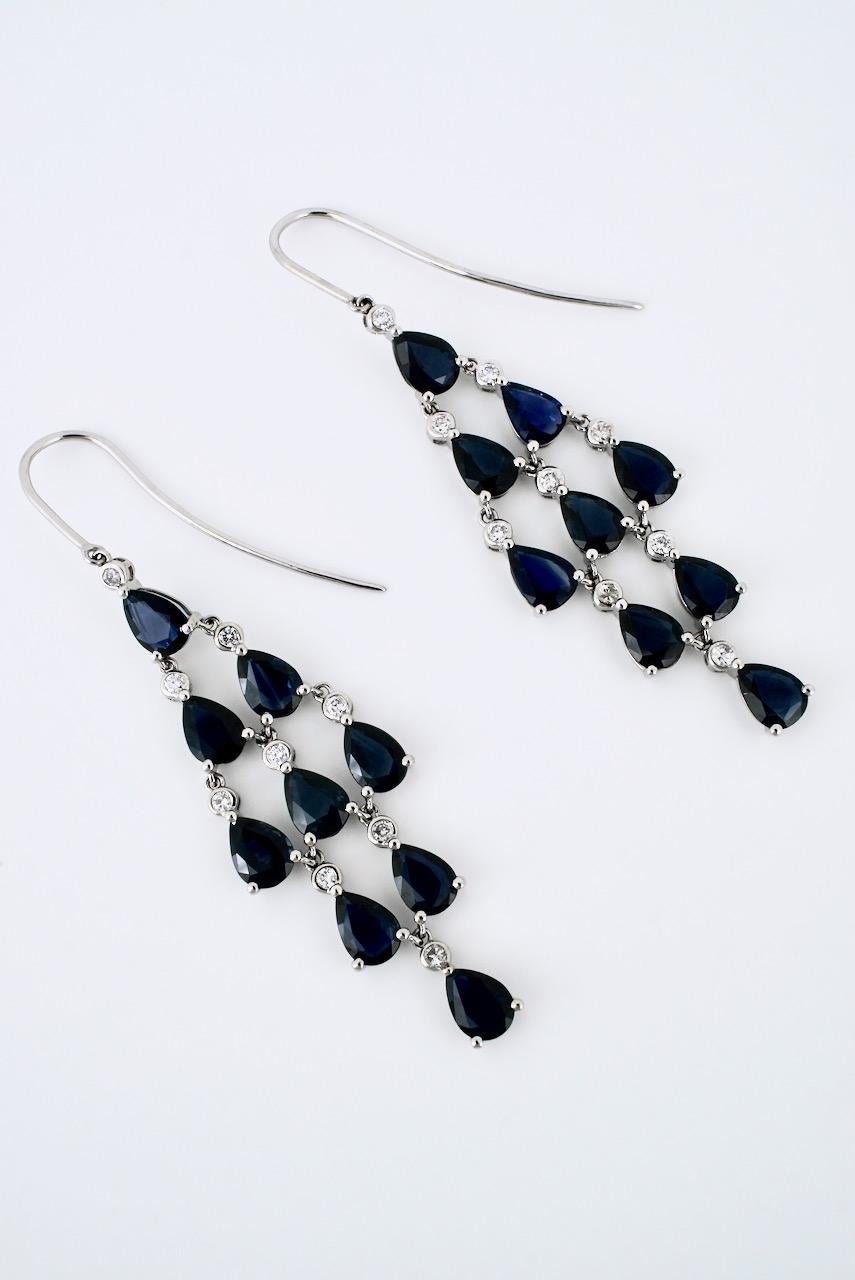 A vintage pair of platinum sapphire and diamond drop earrings with each earring consisting of 9 drop shape dark blue sapphires and 9 bezel set round brilliant cut diamonds arranged into a kite shape chandelier motif and suspended from a hook fitting