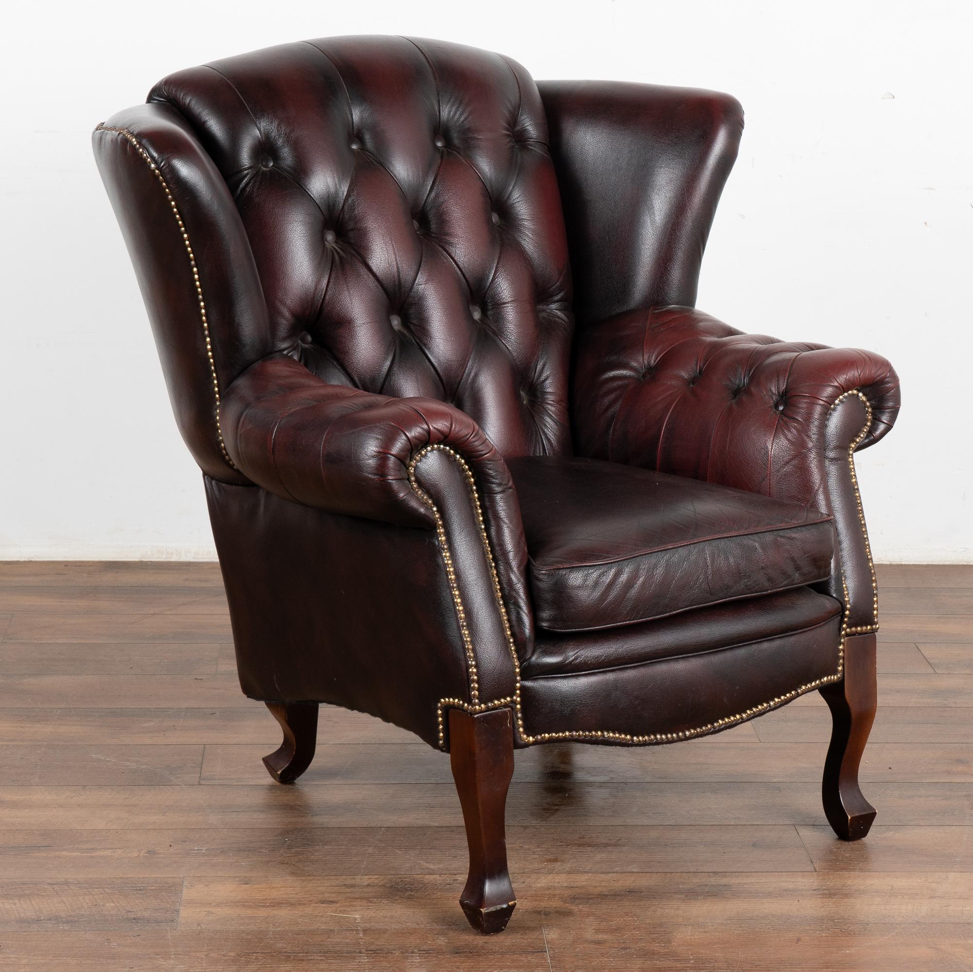 Vintage plum colored leather Chesterfield wingback club chair with aged patina.
Wings, rolled arms, buttons and nail head trim in place. Removeable seat cushion has velcrow to secure in place. 
Sold in solid, vintage used condition; leather and hard