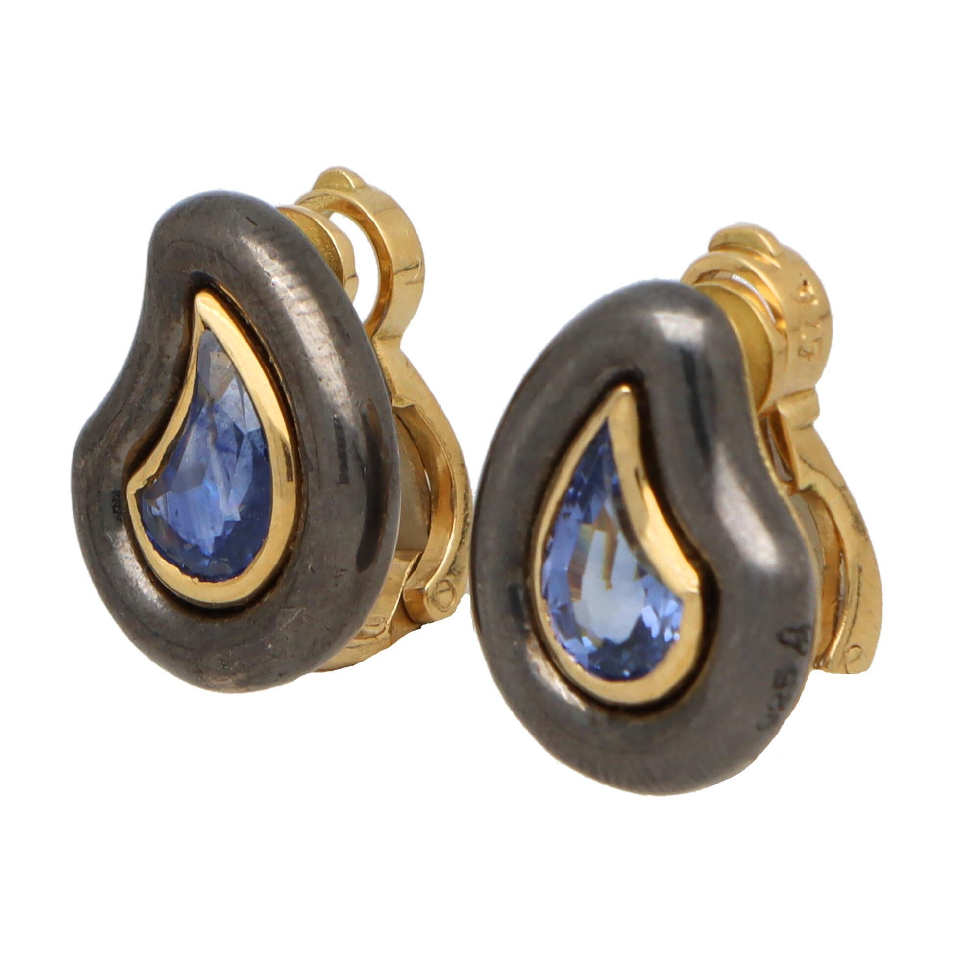 A unique vintage pair of Poiray blue sapphire earrings set in 18k yellow and silver.  

Each earring is predominantly set with a fancy teardrop shape blue sapphire. The sapphires are then rubover set in a yellow gold setting and surrounded by a