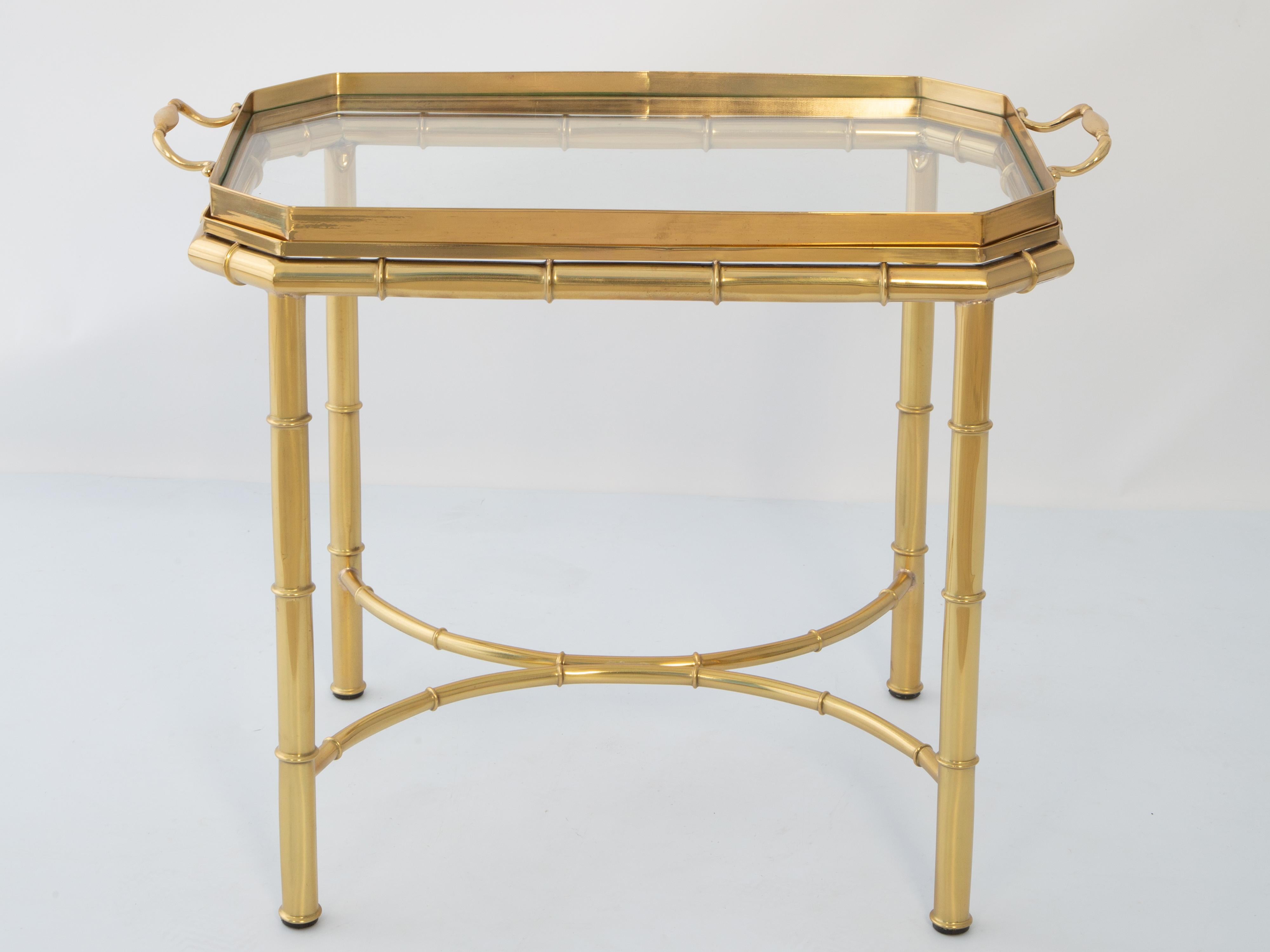 Vintage tea or coffee table of polished brass. Its removable tray top having a rectangular shape with canted corners and handles on each side, its surface inset with glass. Raised on faux bamboo table base of four round legs, joined by double-arched