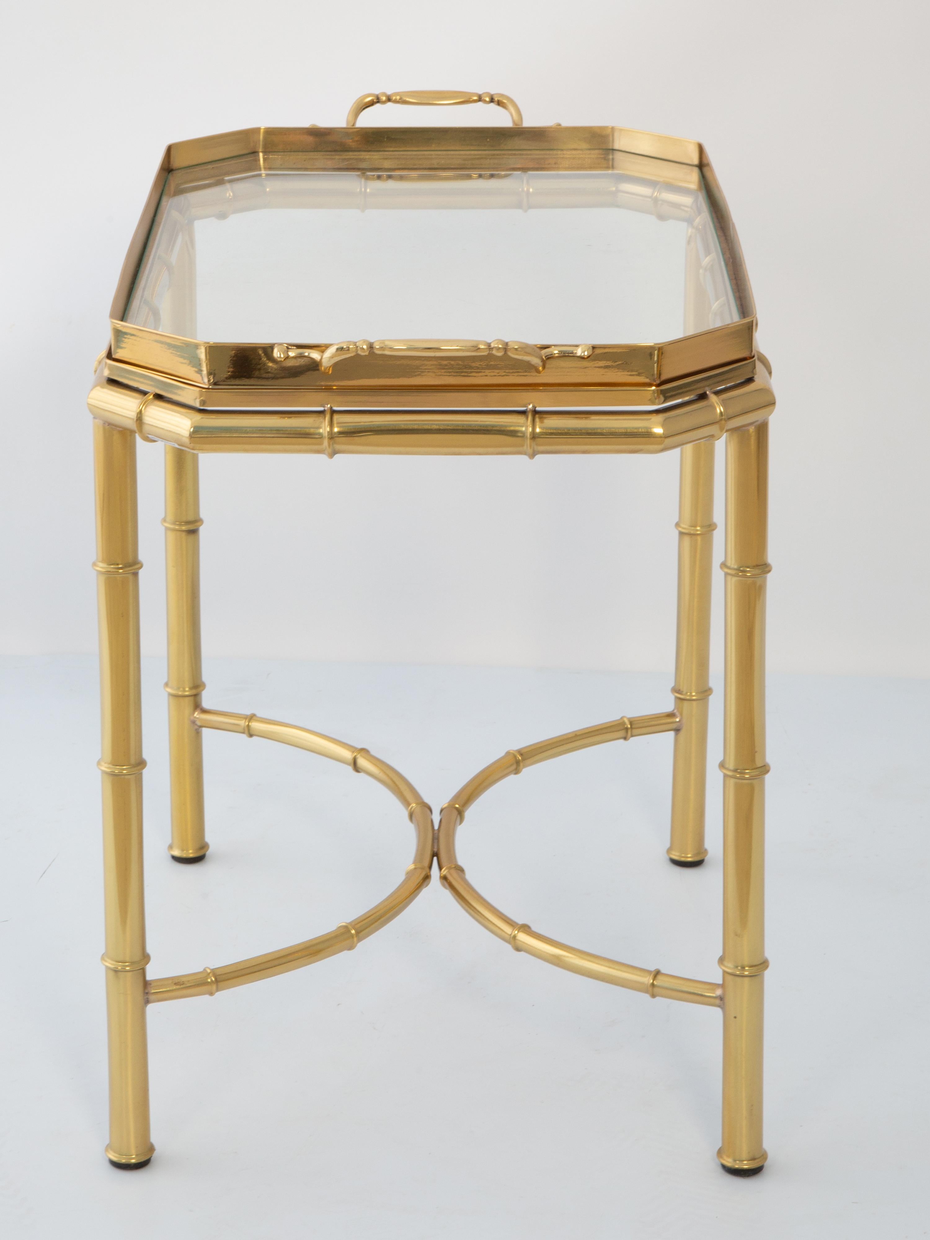 Tavolino da tè o da caffè vintage in ottone lucido. Il suo piano rimovibile ha una forma rettangolare con angoli inclinati e maniglie su ogni lato, la sua superficie è incastonata con vetro. Si erge su una base di quattro gambe rotonde in finto