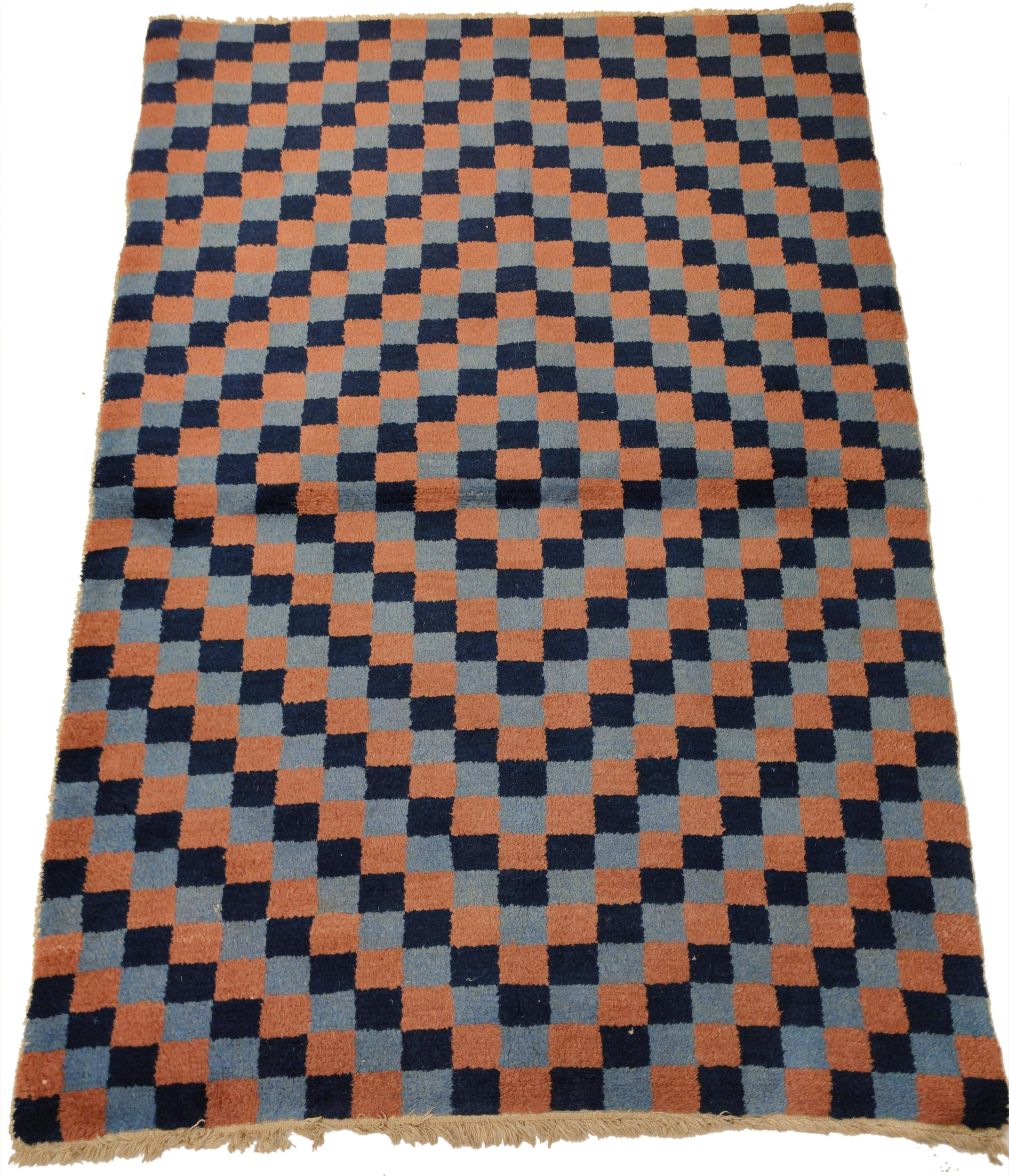 Woven in the khaden format, checkerboard rugs were commissioned in Tibet for monastic use. These are typically woven in two contrasting colours, and more rarely in three colours, like in the present example. These are arranged here in such a way as