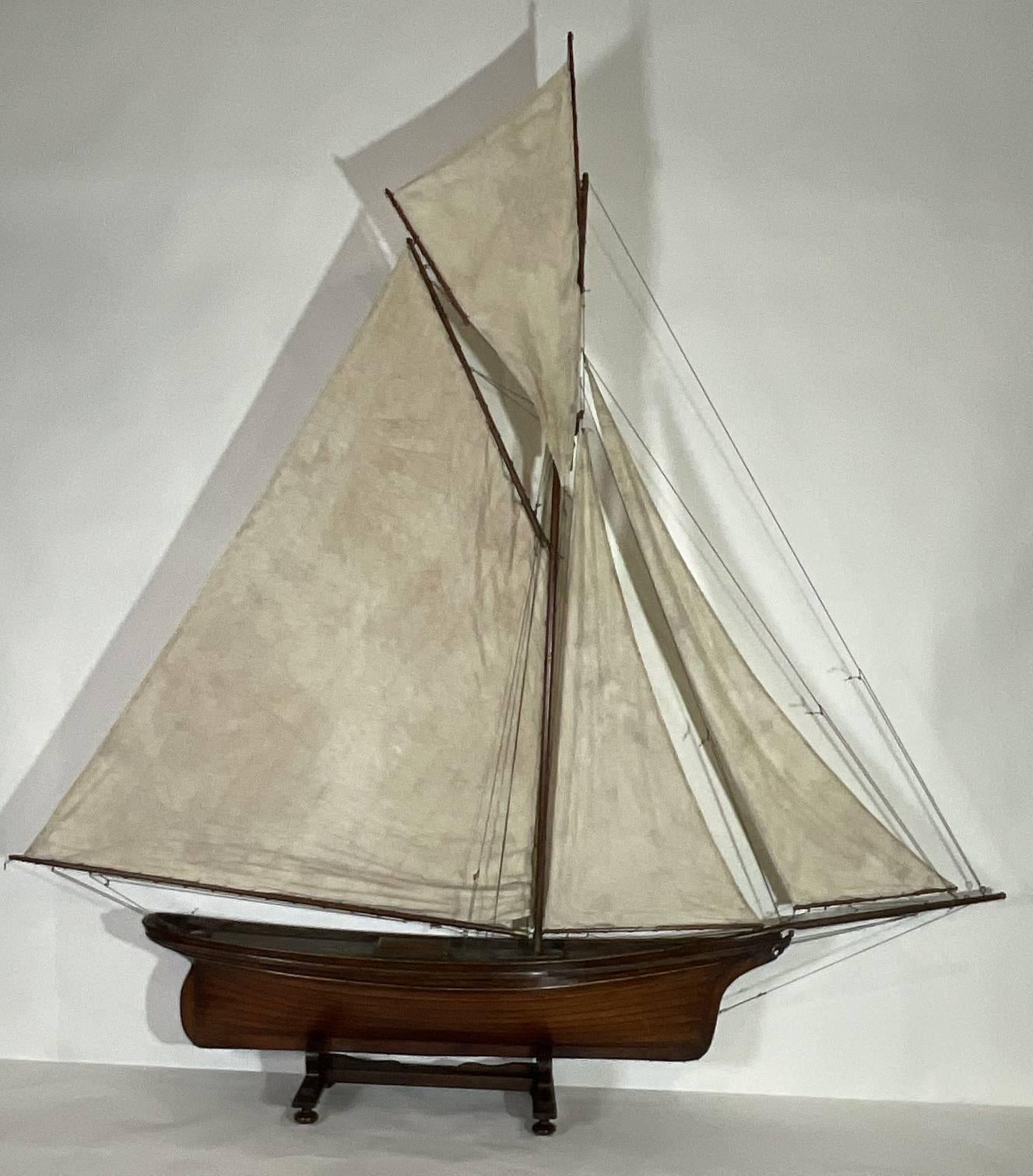 Fine antique clinker built pond yacht. Expertly planked hull. Canvas covered deck is painted green. Nice suit of linen sails. Fully rigged. Many brass fittings gaff rigged with a flying club sail. Wood cradle. Brass makers badge at the stern is