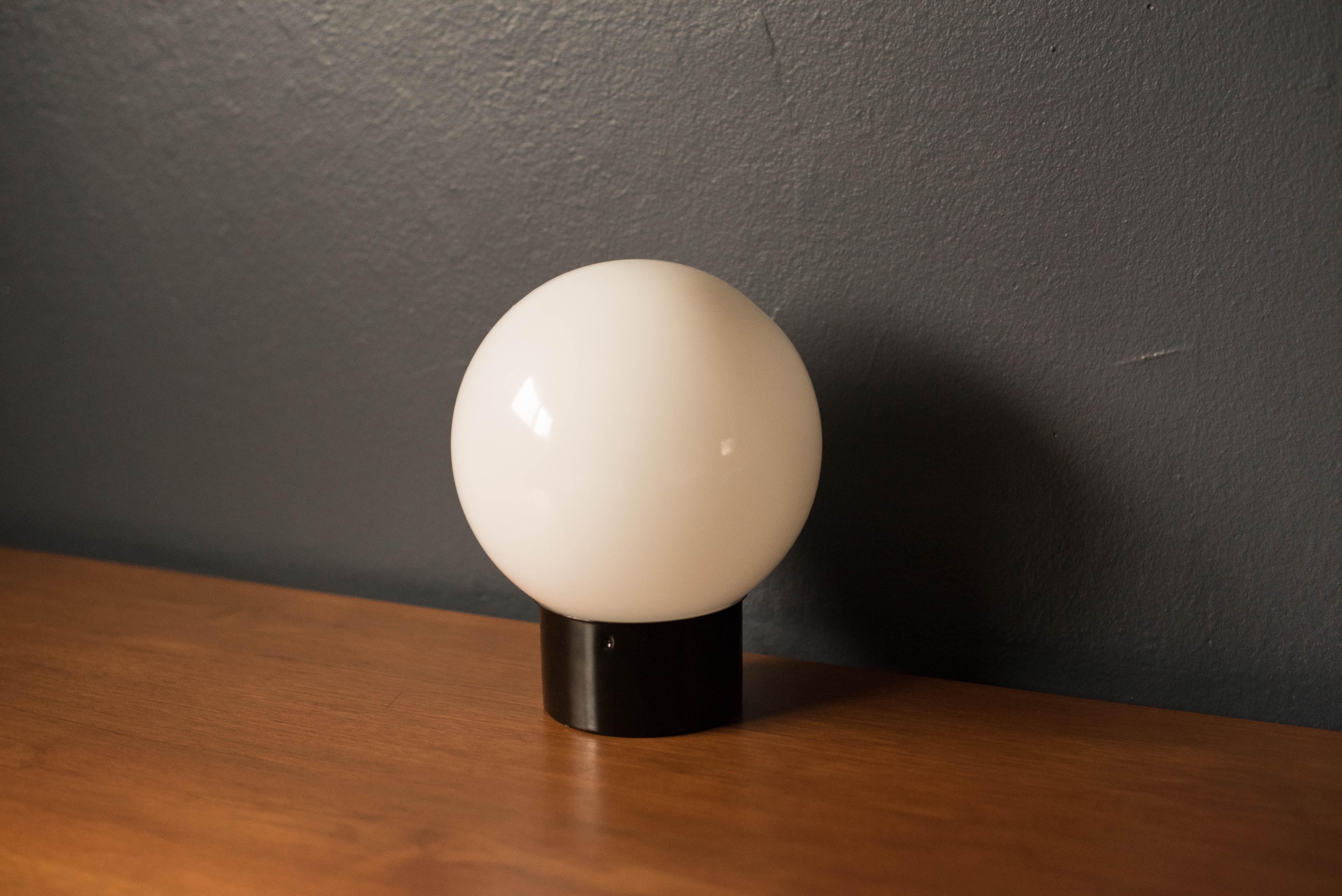 Vintage pop art mod lamp, circa 1970s. Round glass globe sits on a black cylinder base and emits a glowing light. Recommended to use as a table lamp for an office desk or accessorize any home decor.

   