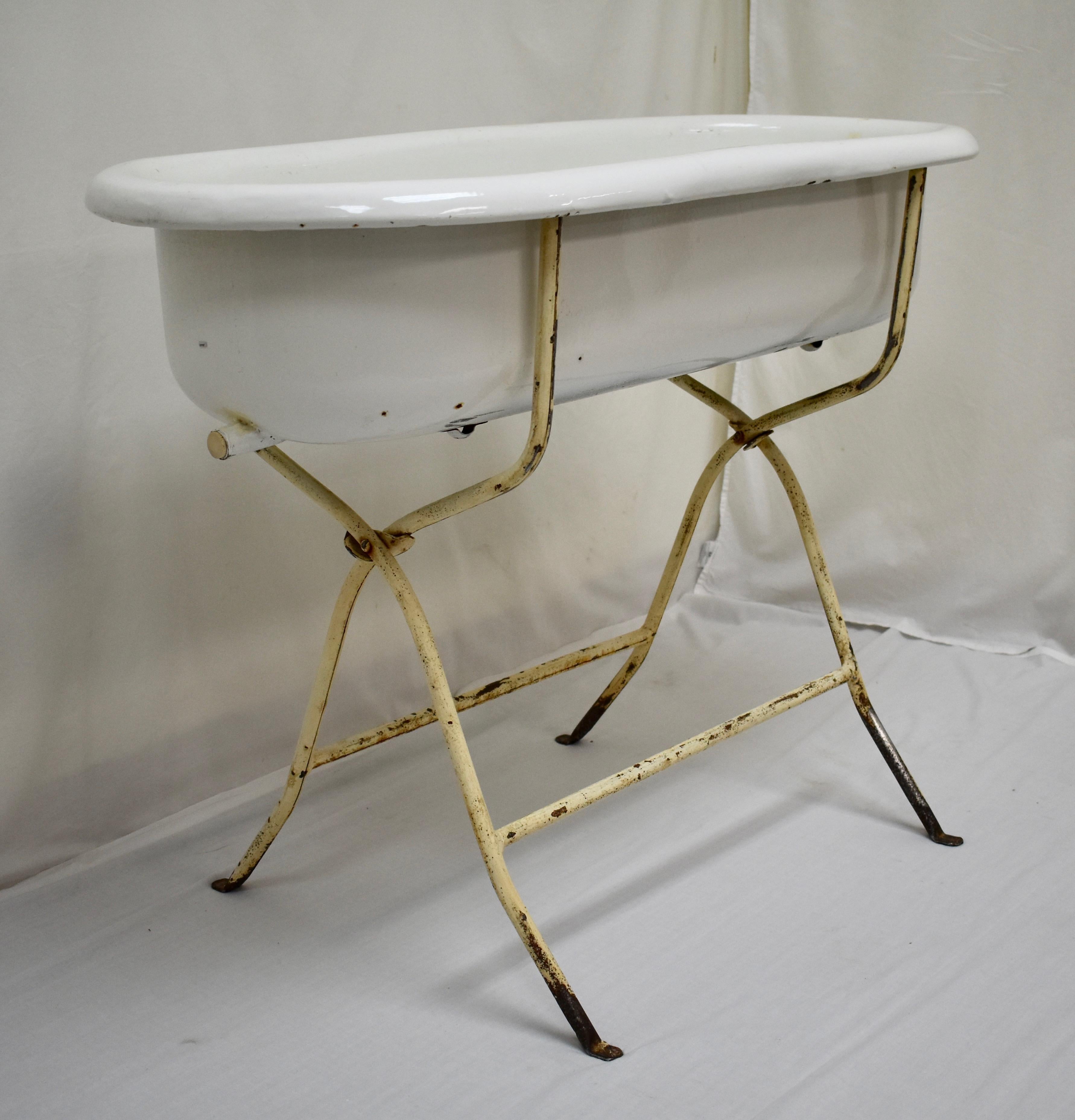 This is a vintage porcelain enamel baby bath on its original wrought iron folding stand. These are great for putting beer or wine on ice for a party, for planting and landscaping, or even for bathing the baby. This piece has a cork to replace the