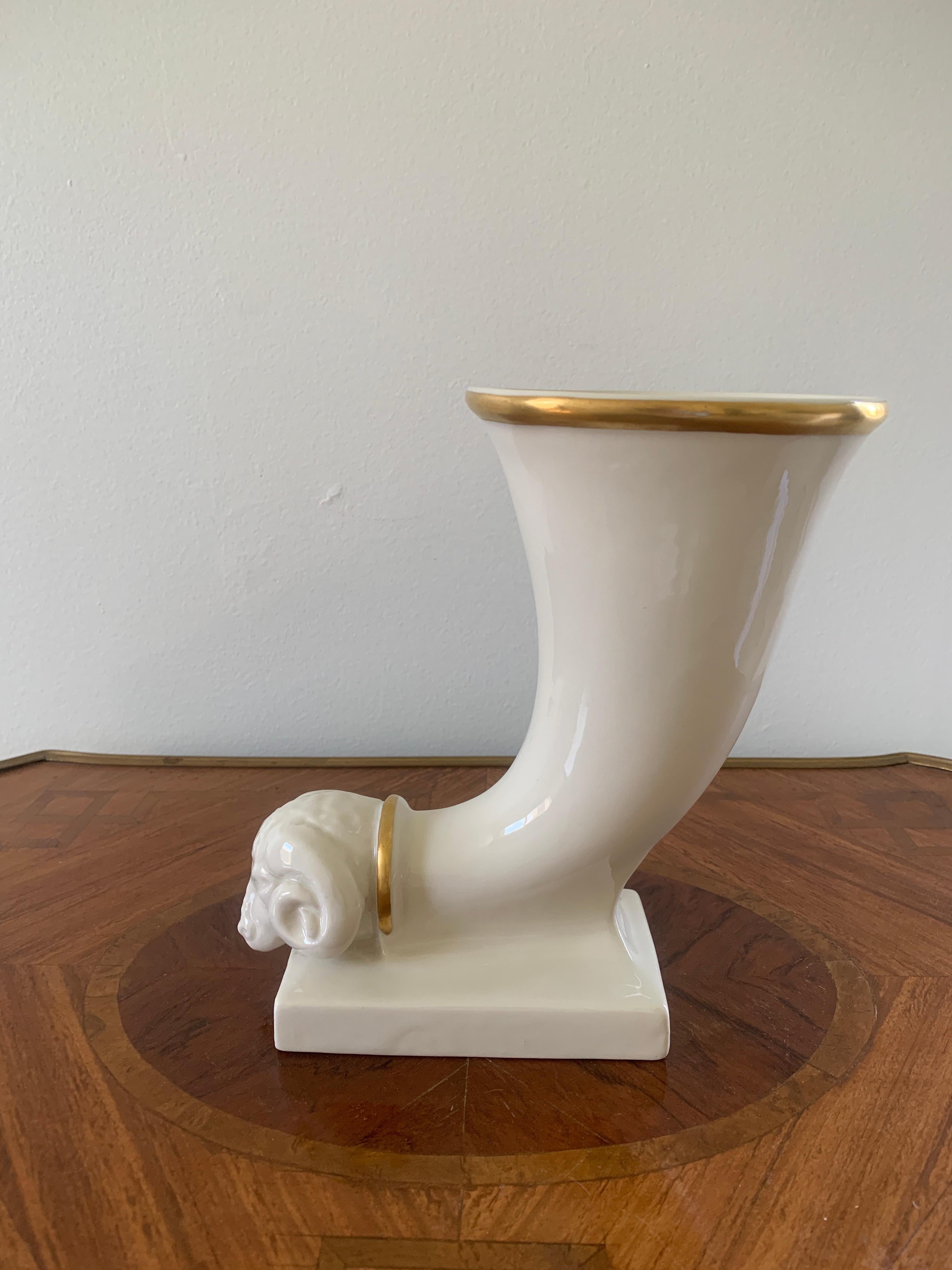 A beautiful neoclassical style cream colored porcelain cornucopia vase with a ram's head and hand-painted gold details.
