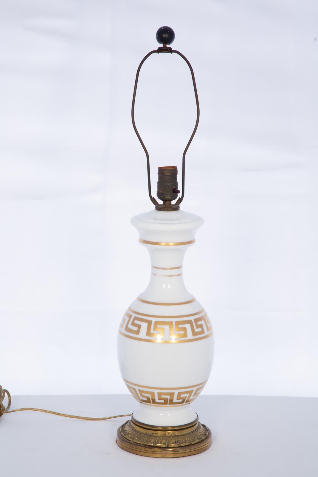 Single porcelain table lamp, having a vase shape of white glass, gilt decoration of two Greek key meanders wrap the body of the lamp, raised on round brass base.

Stock ID: D4014