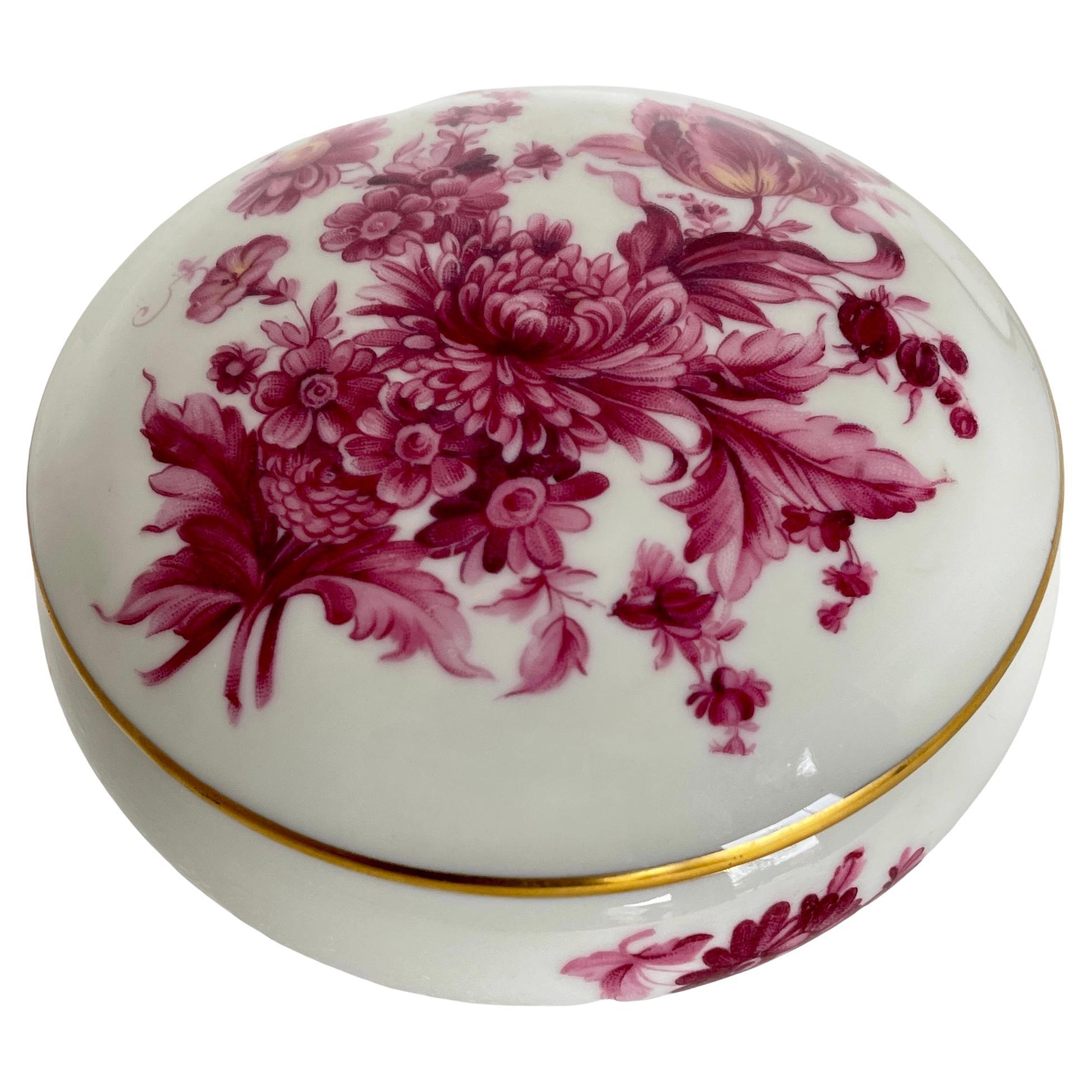 Vintage German porcelain vanity box. This petite round box has gorgeous hand painted detail throughout lid and body of box. The floral design is in striking magenta colors with gold banding between the lid and body of the trinket box. The interior