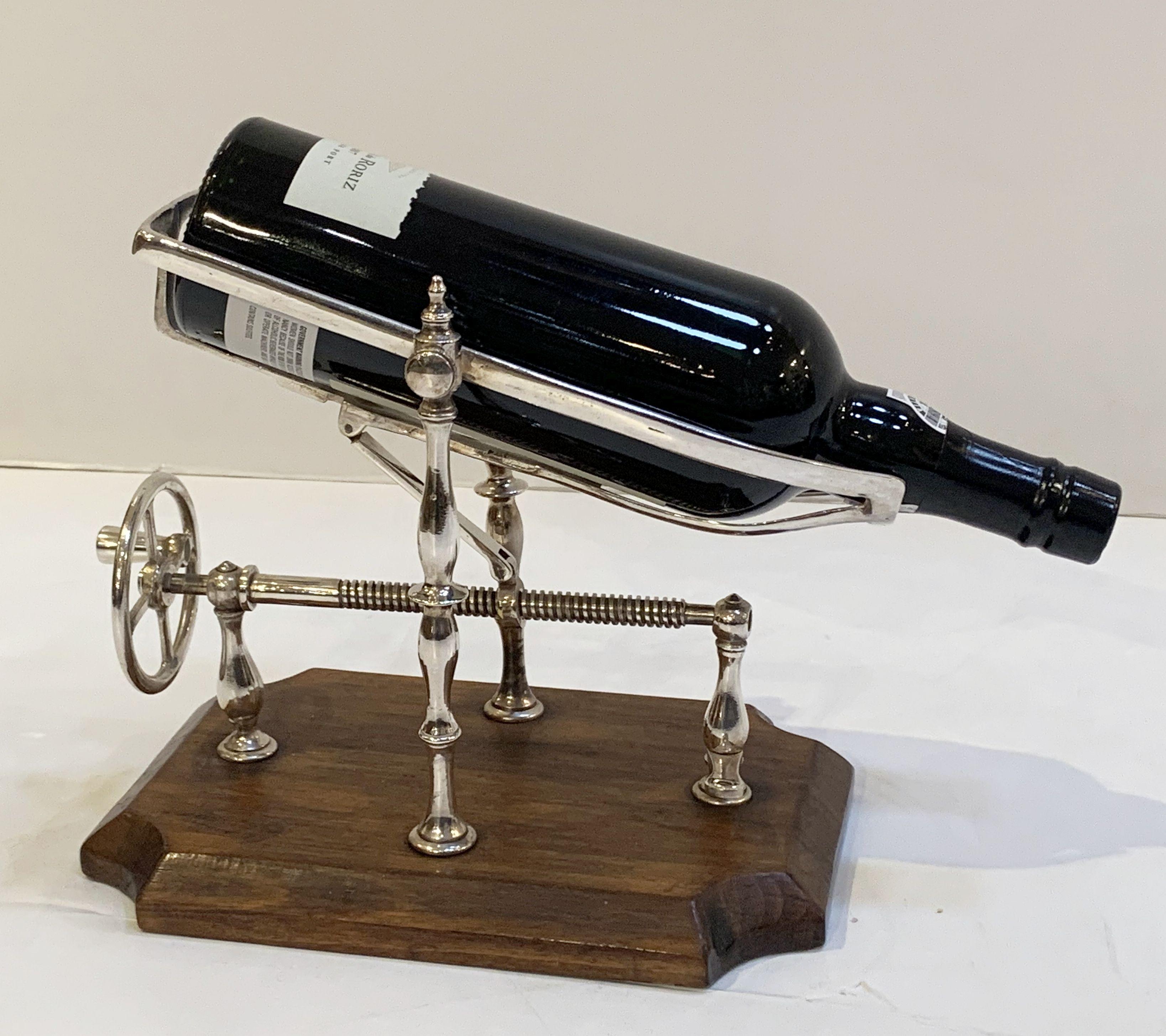 A handsome English port decanter or wine bottle pourer of silvered or chromed metal with turn screw action, on moulded rectangular wooden base.

A mechanical spirits pourer or decanting cradle is an artisan-like decanting device - turning the screw