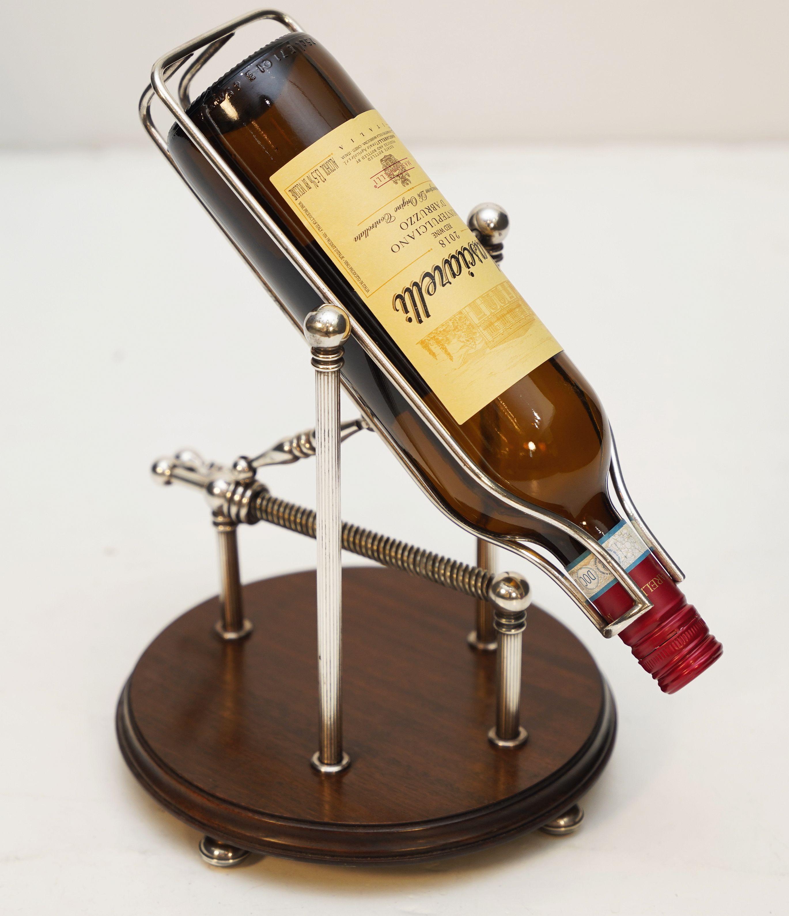 A handsome English port decanter or wine bottle pourer of silvered or chromed metal with turn screw action, on moulded round or circular wooden base with ball feet.

A mechanical spirits pourer or decanting cradle is an artisan-like decanting device