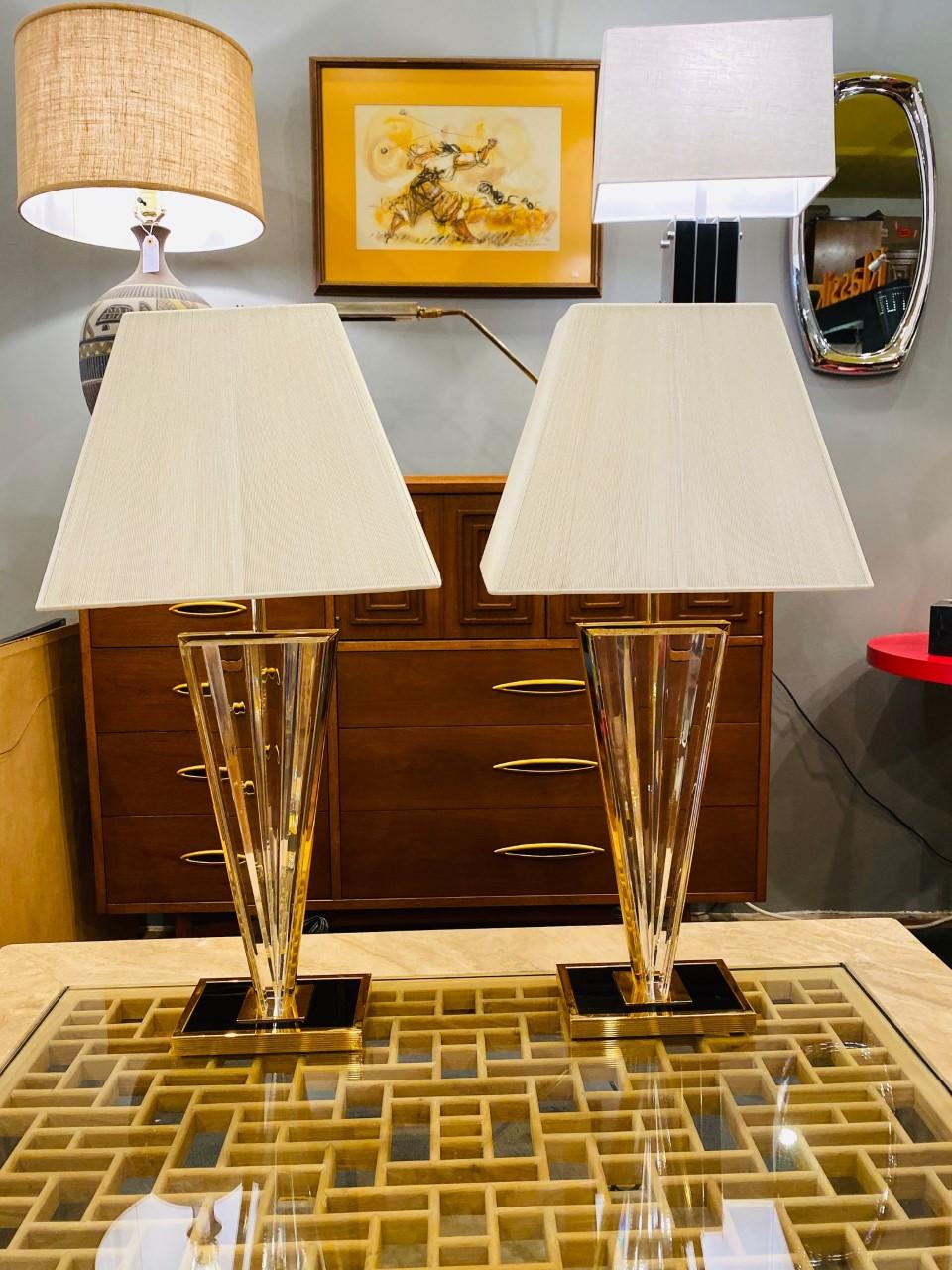 Striking and glamorous, this pair of table lamps exude a graphic element of style, yet, transmutable in form, they can relay to their minimalist essence for a more linear and clean aesthetic. The base is defined in black and gold metal with the