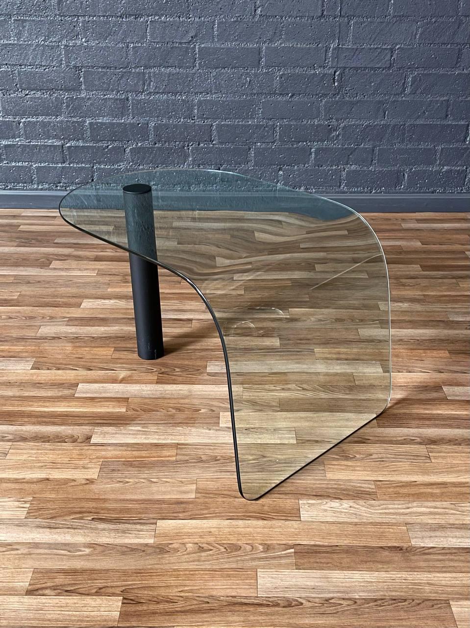 Condition: Original Vintage Condition

Materials: Curved Glass, Metal Base

This sculptural Post Modern glass table from the 1980s features a striking waterfall design crafted from a single curved pane of glass. Anchored by a bold cylindrical metal
