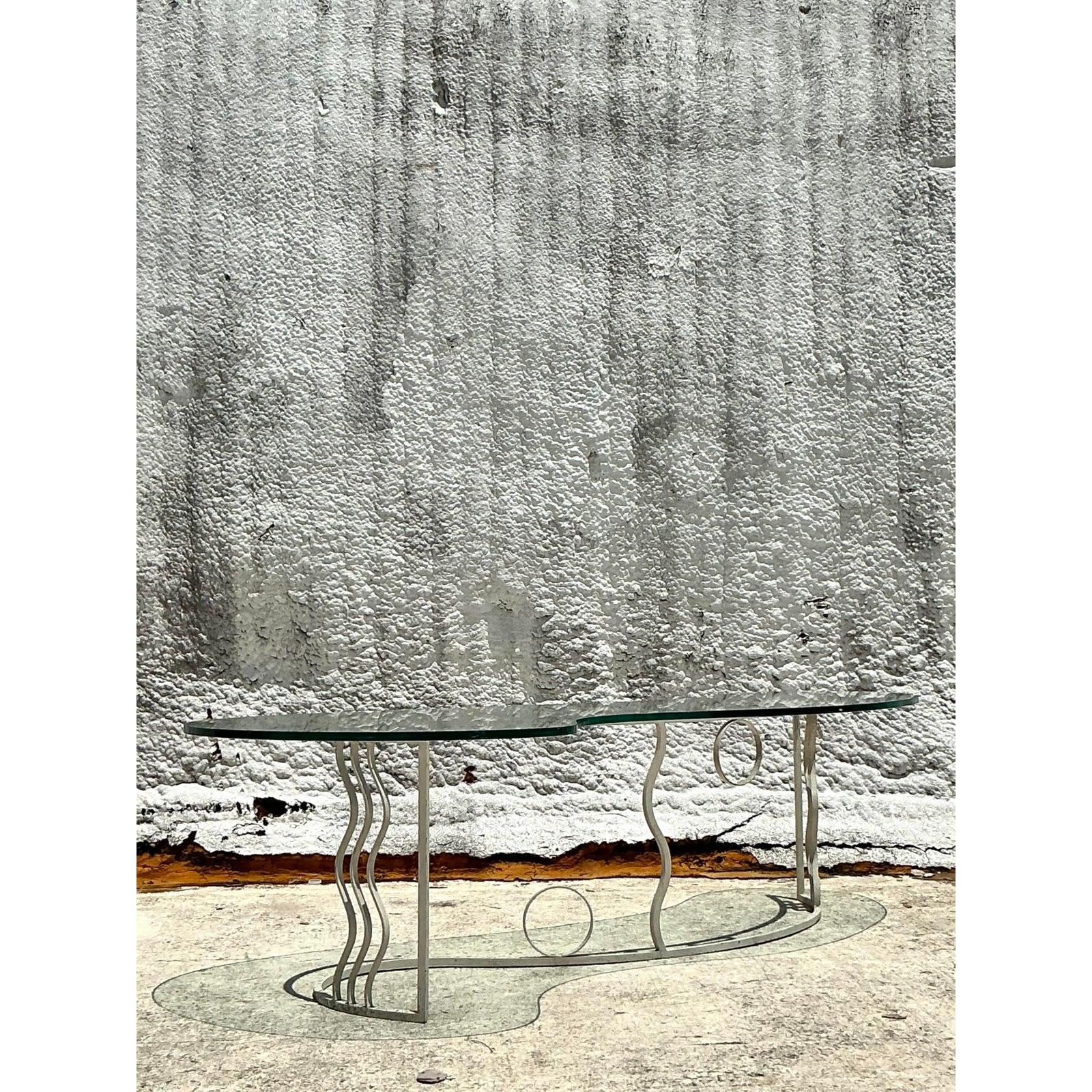 Capture the bold, artistic spirit of the 1980s with this stunning postmodern coffee table. This piece is a true work of functional sculpture, featuring a freeform, biomorphic glass top that appears to float above its dynamic base. The powder-coated