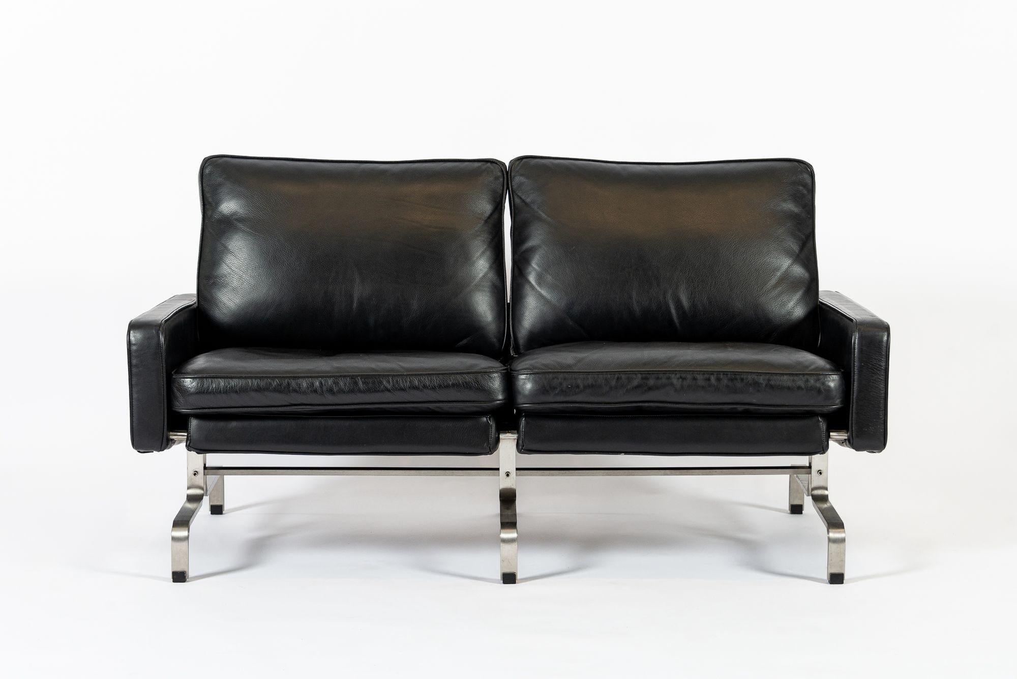 This incredible vintage postmodern black leather loveseat couch in the style of Poul Kjaerholm is circa 1980. The unique two-seat loveseat sofa is sturdy and well-built with a clean, minimalist aesthetic and a brushed flatbar steel base. The
