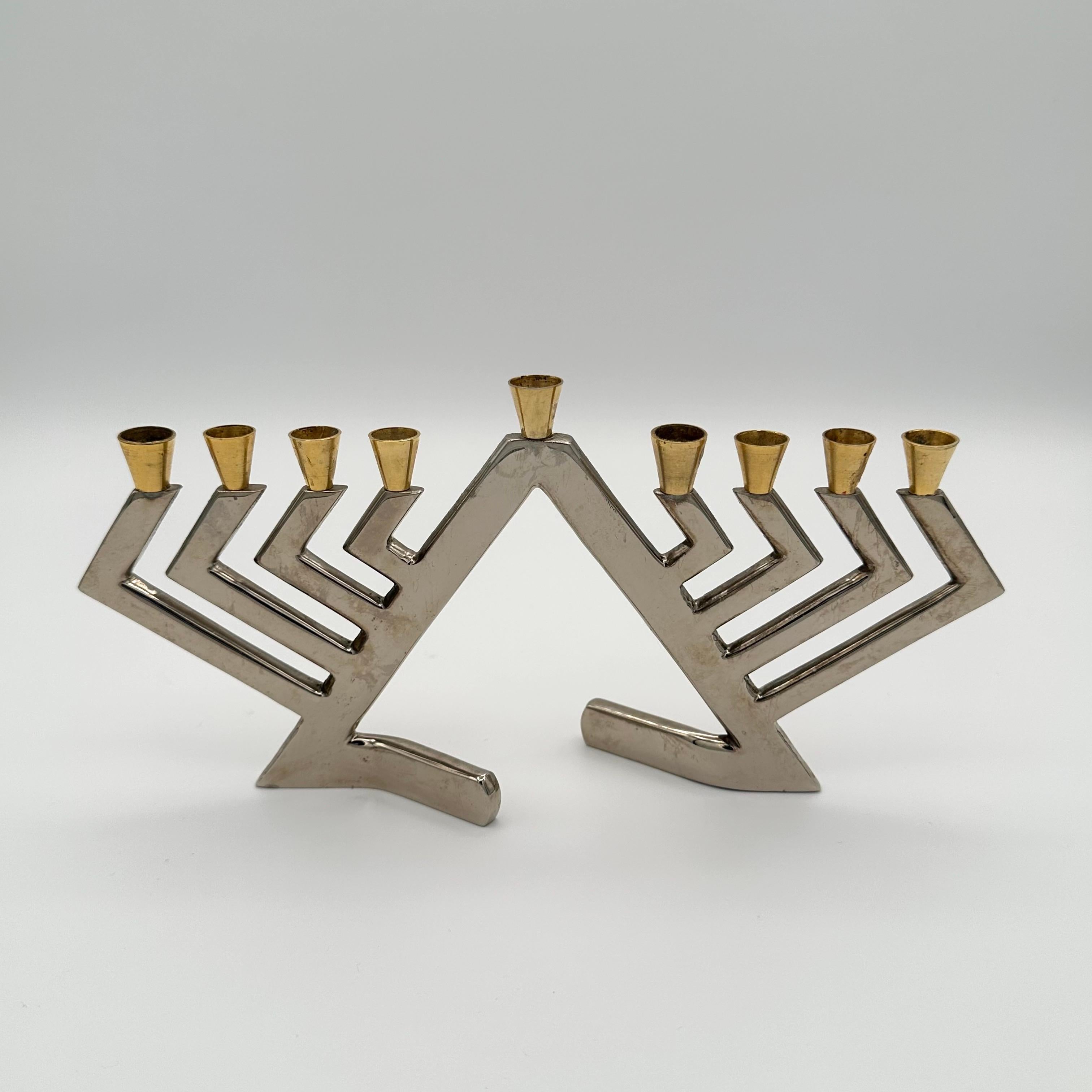 Vintage Chanukah Menorah in chromed steel and brass with a geometric form that evokes Brutalist, Postmodern, and even Art Deco skyscraper styles. Angular and zig-zagging chromed steel arms support flared brass candleholders. Signed on one of the