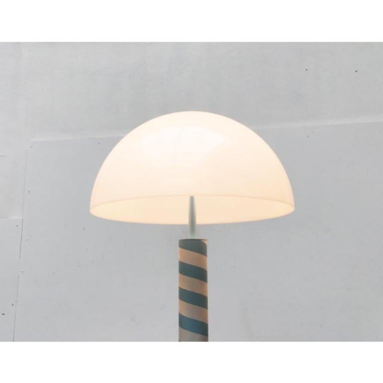 Lámpara de pie posmoderna con un llamativo diseño.

Llama especialmente la atención el sensacional dibujo y la combinación de colores en azul claro y blanco alternados. La pantalla semiesférica es de plástico translúcido. La base pesada está