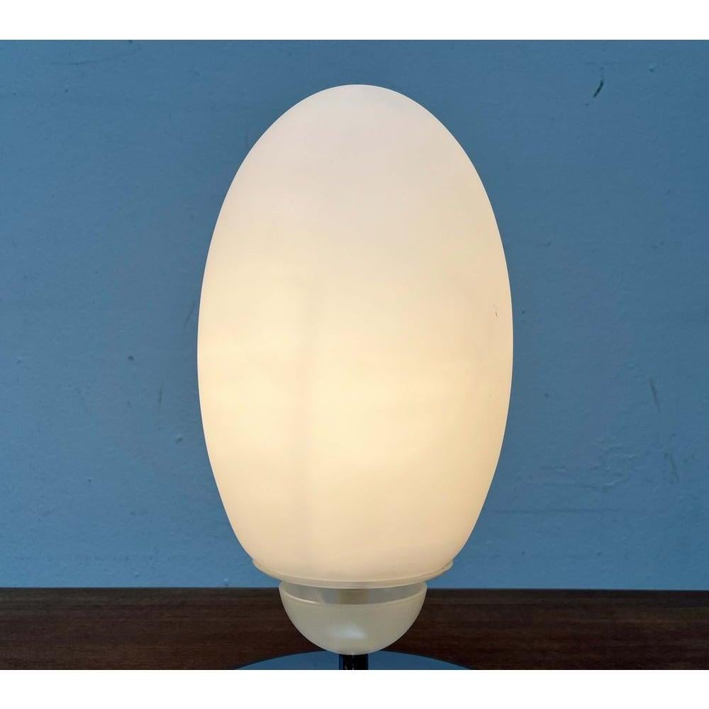 La version lampe de table de la série Brera de Flos, conçue par Achille Castiglioni.

Une lampe de table très simple et élégante en verre et chrome. Le corps de la lampe en verre opale de forme ovoïde repose sur une courte et fine tige en métal