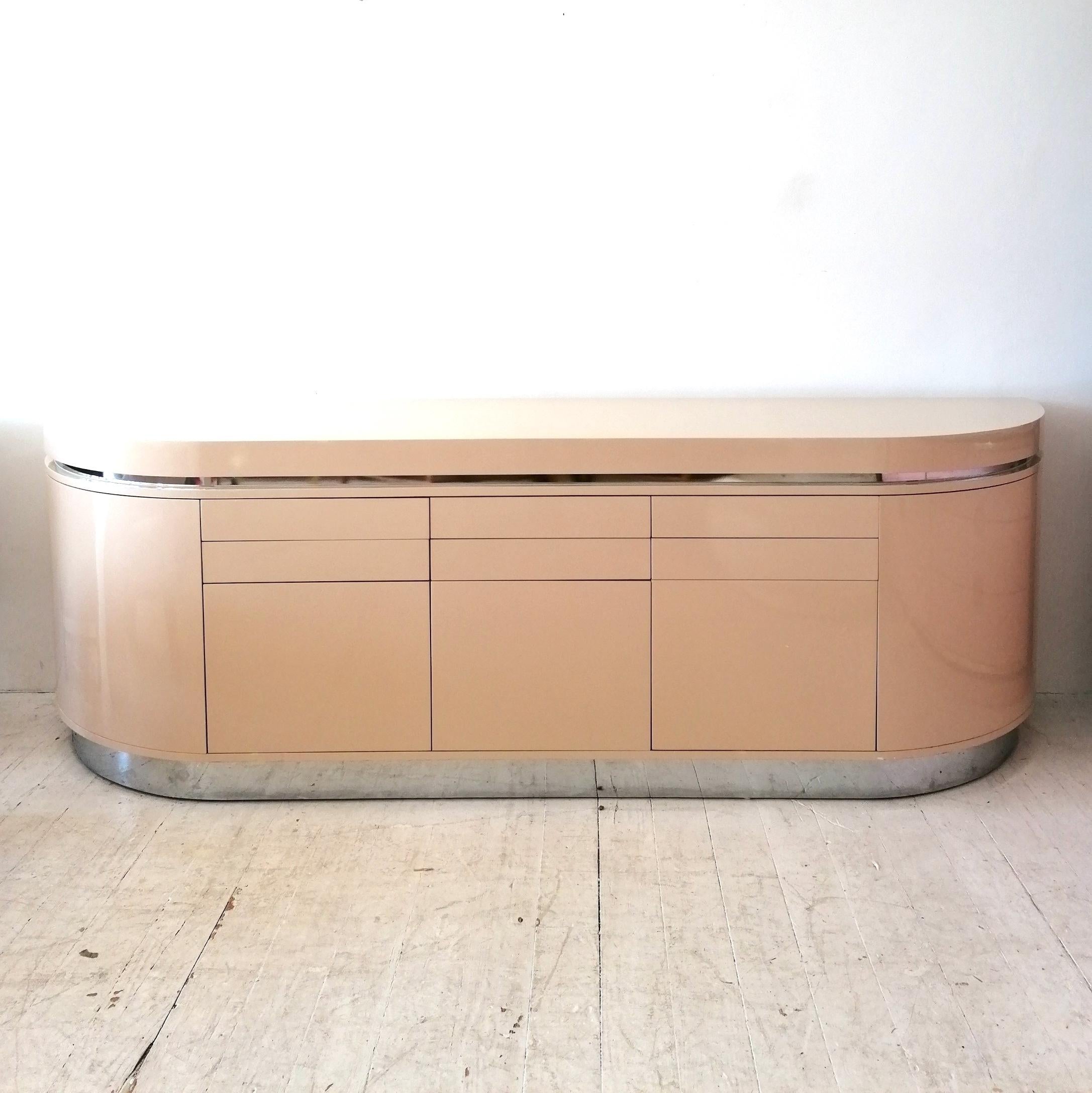 A substantial & super quality deep warm cream lacquer curved demi-lune sideboard by J. Wade Beam for Brueton, USA, 1980s. An excellent example of 80s postmodern deco revival design. Adding to the streamlined look is an inset band of chromed metal,