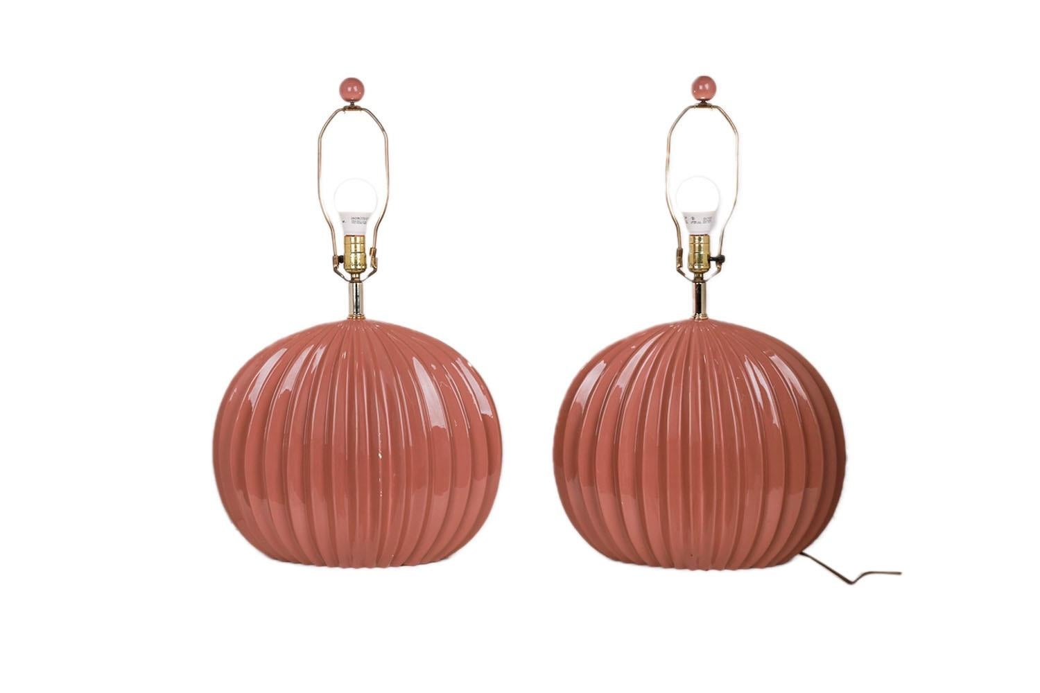 A beautiful pair of post-modern, flattened sphere-shaped ceramic table lamps with original empire shape shades, circa 1980s. They feature a striking high gloss dusty rose or mauve glaze shell-like body adorned with a sculptural ribbed pattern, each