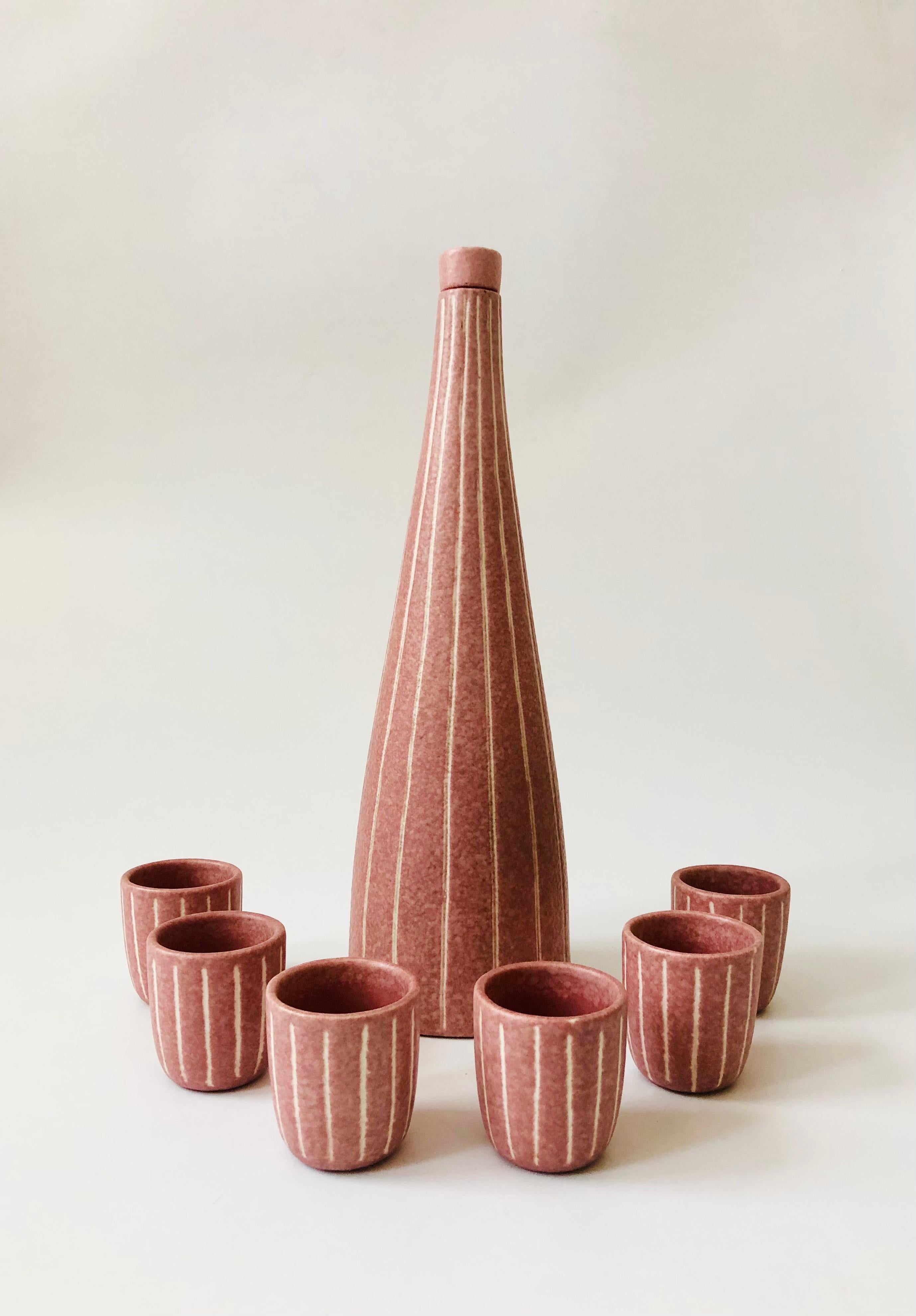 A rare 1980s postmodern pottery decanter set made by Jaru of California. Includes a tall conical decanter with stopper and 6 matching cups. Each piece has been decorated with carved vertical white stripes that contrast with the pink base