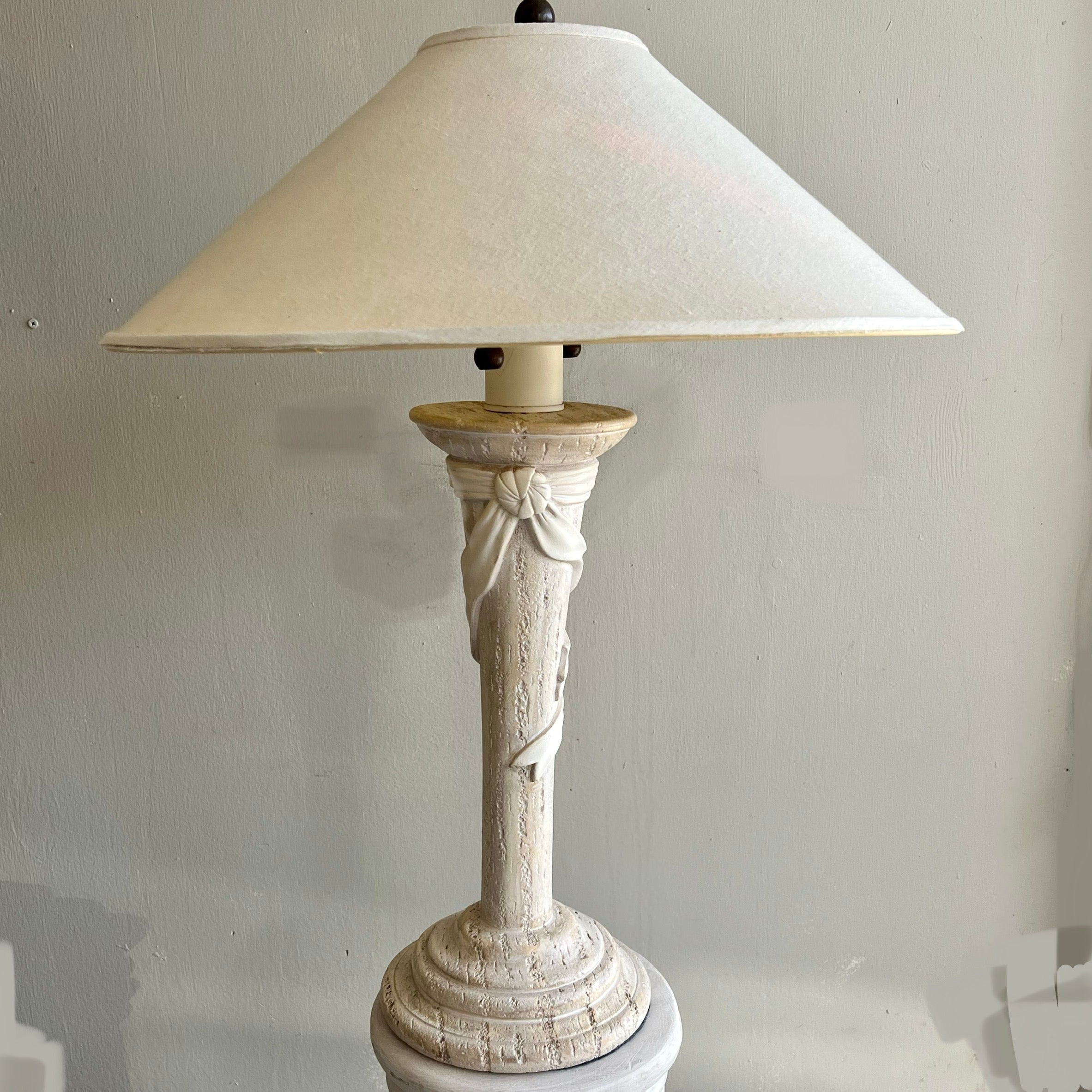 Exquisite sculptural plaster table lamp tied with a “ribbon.” Faux travertine plaster and fine detailing. Excellent condition. The included lampshade has a few ridges but can easily be replaced if desired. Has two bulb sockets, each with their own