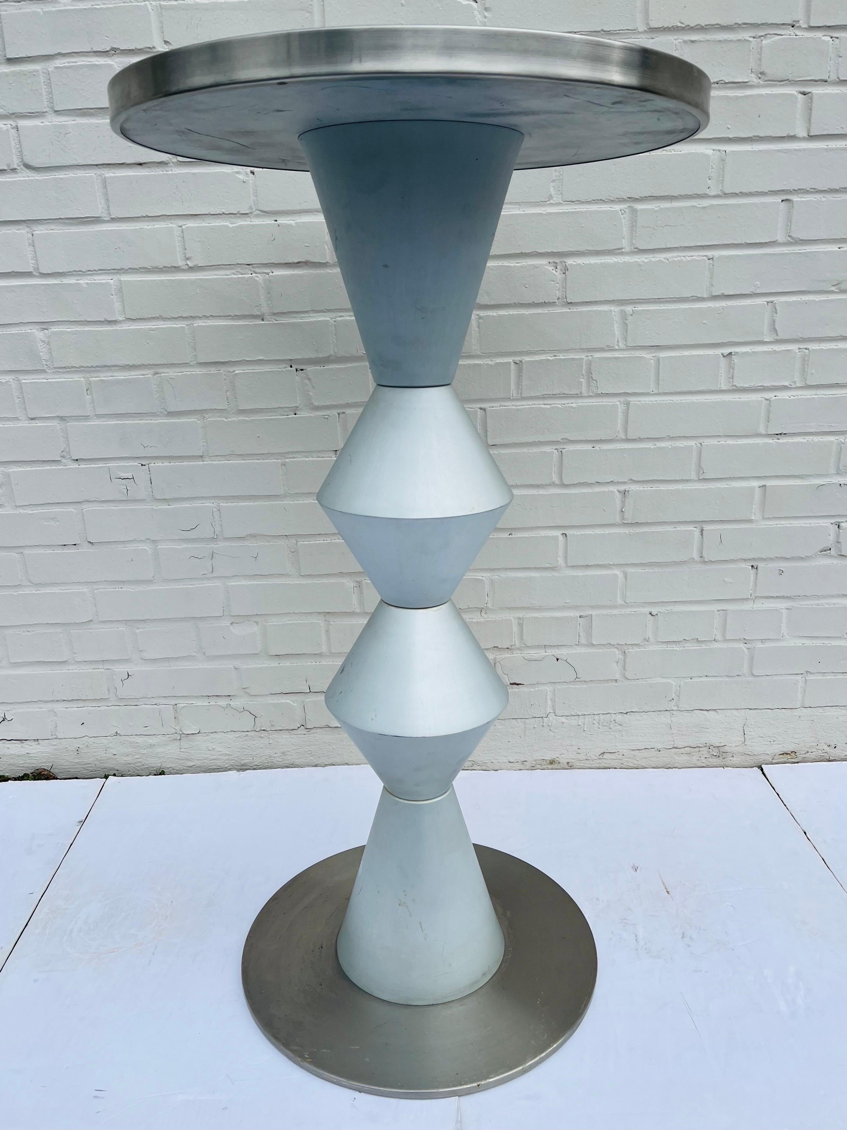 A vintage post modern style high round table in aluminum and stainless steel. The round, stainless steel top is complemented by the brushed aluminum shaft. The sculptural design of the table upright is reminiscent of the abstract works of Constantin