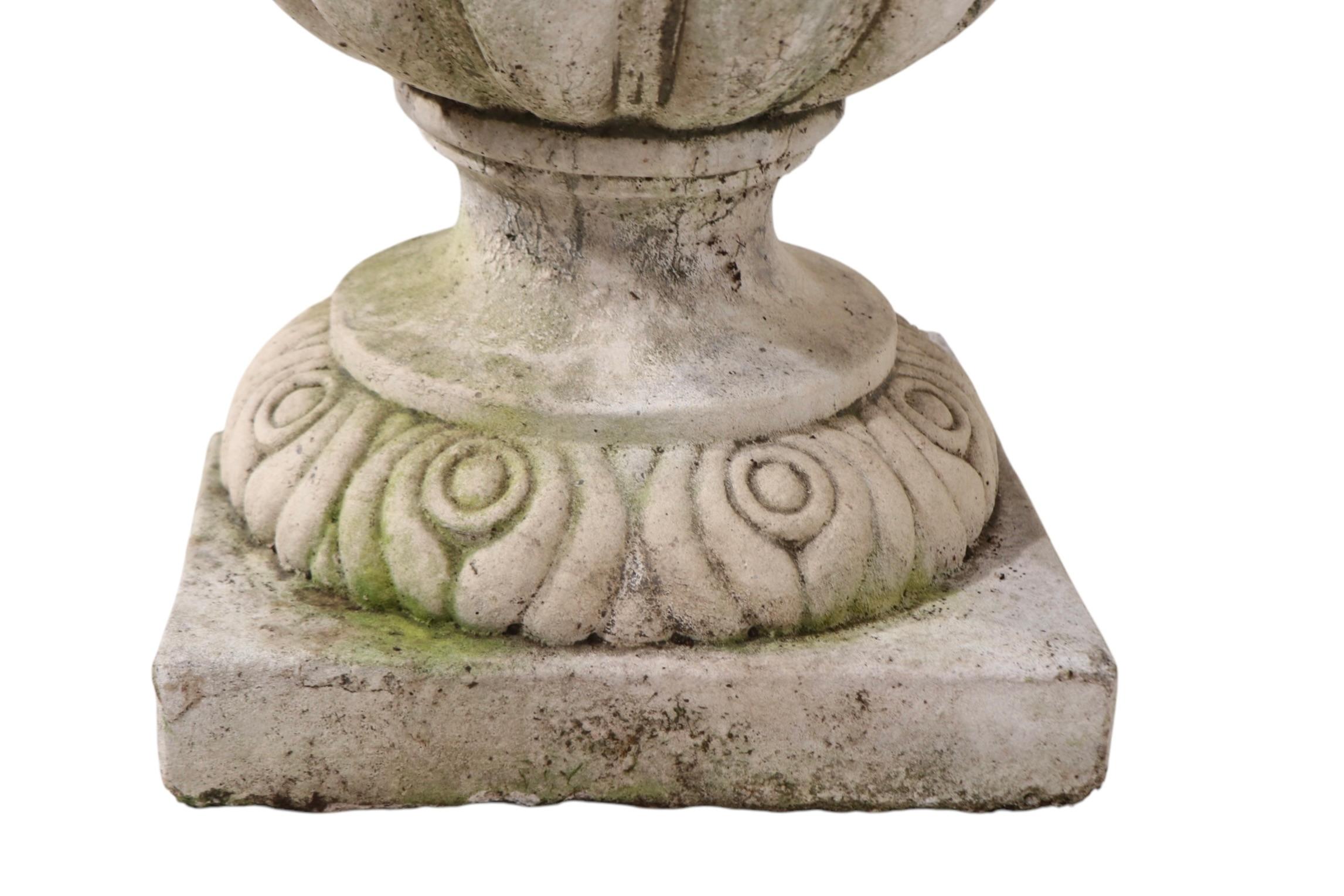 Exceptional urn form planter in poured stone with great patina and surface. The urn features a big deep bowl with foliate decoration, two handles each with a face. The urn planter has a decorated pedestal with a square plinth base. This example is