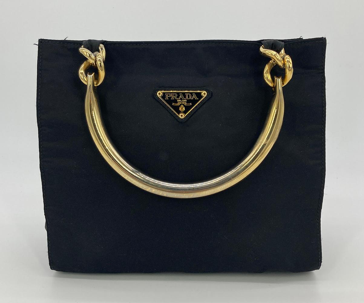 Vintage Prada Black Nylon Gold Handle Bag in very good condition. Black nylon exterior trimmed with gold hardware. Top zipper closure opens to a black nylon interior with one zipped side pocket. Overall good condition. some wear/tarnish on handles-