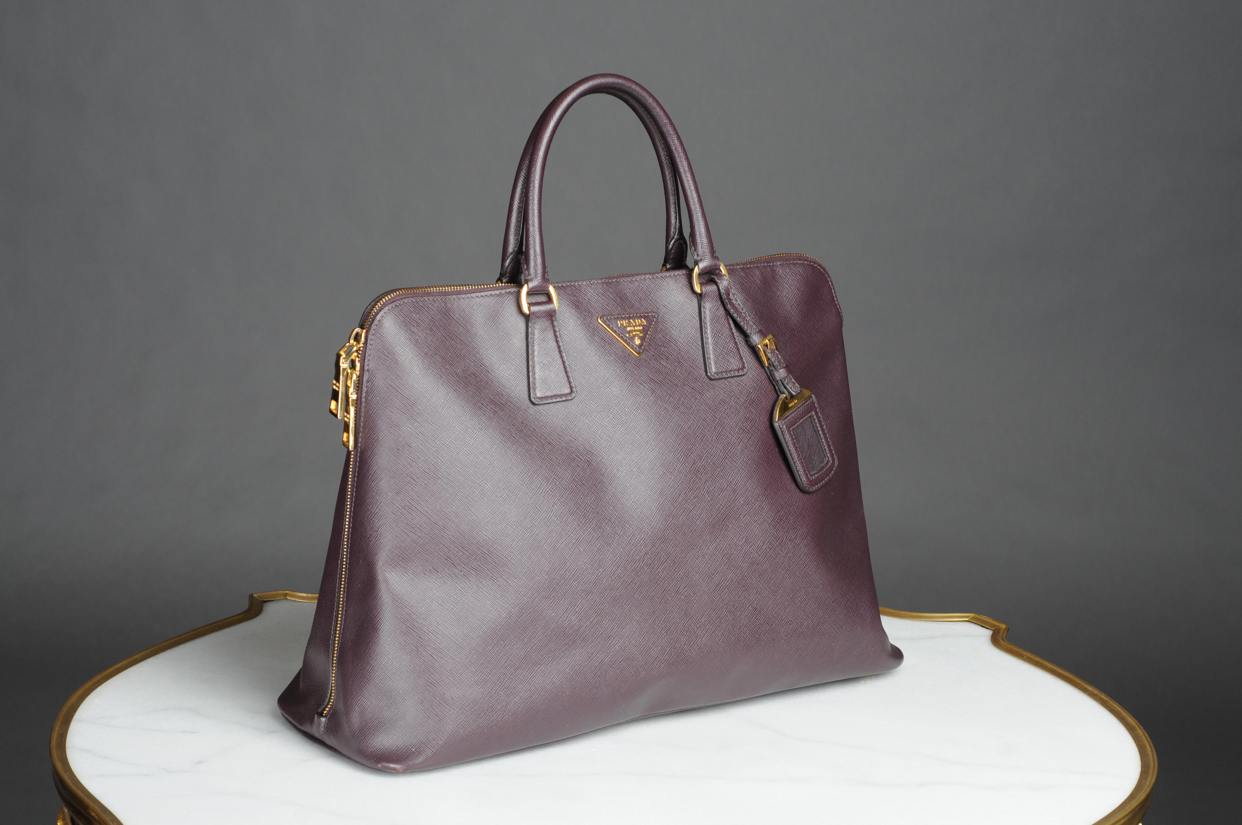 Prada Purple Saffiano Lux Leather Promenade Bag This stunning promenade bag impresses with its appeal and style. The bag shines in an elegant dark purple tone, is made of leather and has two rolled handles. The zipper leads to a nylon interior with