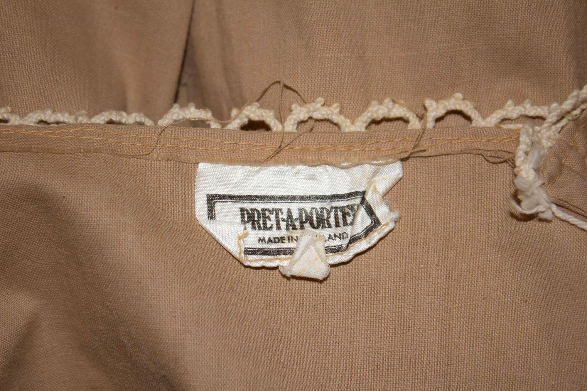 Ein lustiges langes Vintage-Kleid von Pret a Porter . Das Kleid aus karamellfarbener Baumwolle hat eine durchgehende Knopfleiste mit Spitzendetails und eine Rüsche am Saum.  Maße: Büste 34'', Länge 57''