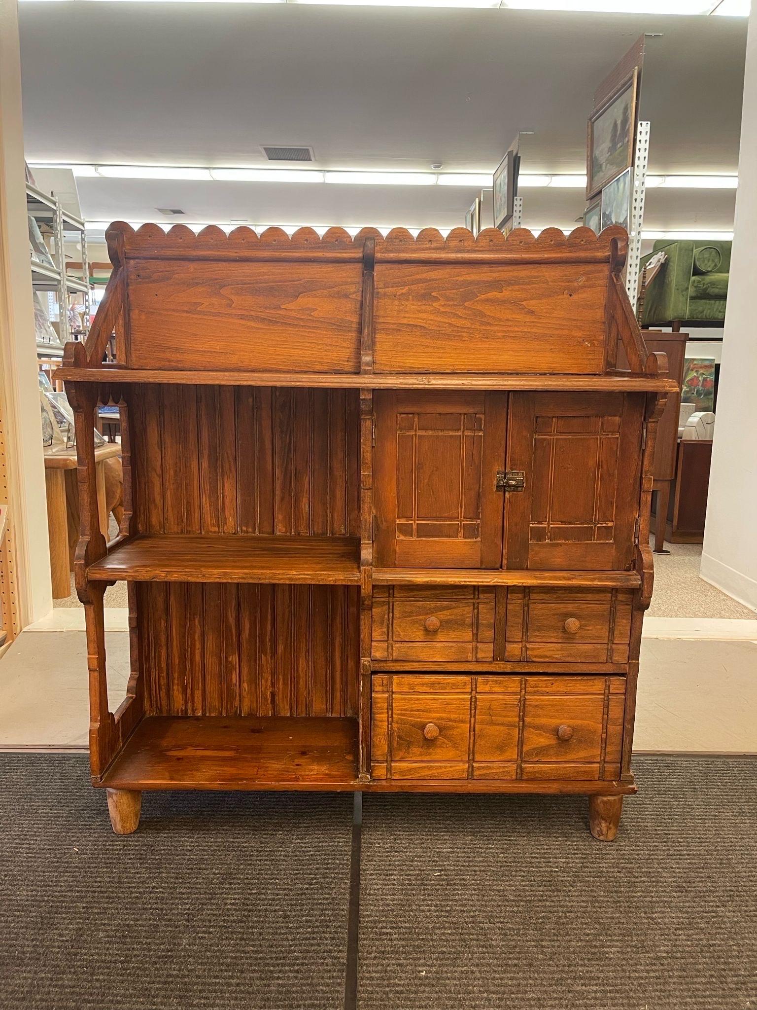This bookshelf unit has handmade caved wood detailing everywhere. The top is scalloped detailing , that matches the detailing on the sides. The cabinet space has original hardware on the front. Three drawers with turned wood handles. Rustic design.
