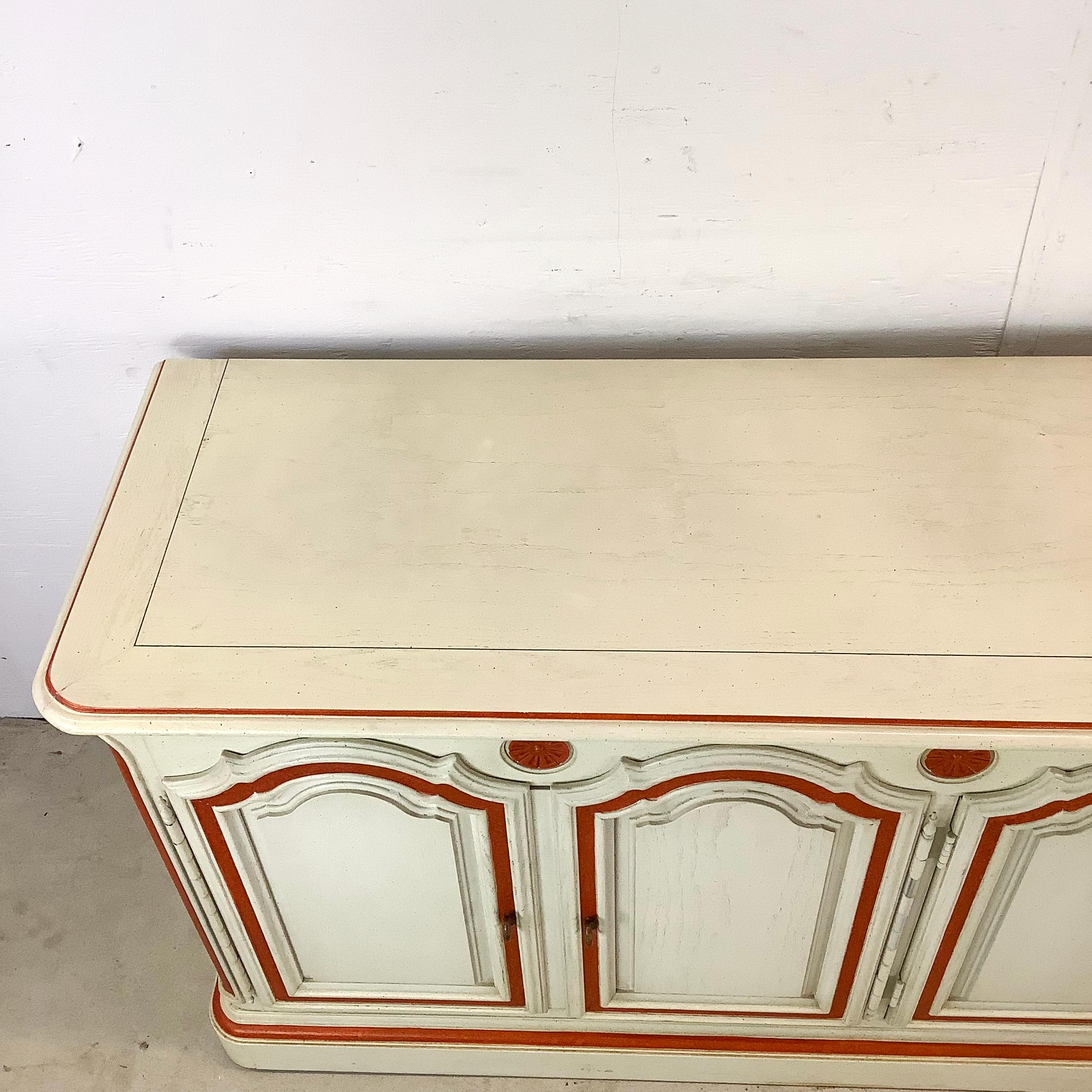 Holen Sie sich die sonnenverwöhnte Schönheit Südfrankreichs in Ihr Zuhause mit diesem Sideboard im provenzalischen Stil. Seine charakteristische cremefarbene Lackierung und die von Hand aufgetragenen orangefarbenen Verzierungen sind ein auffälliges