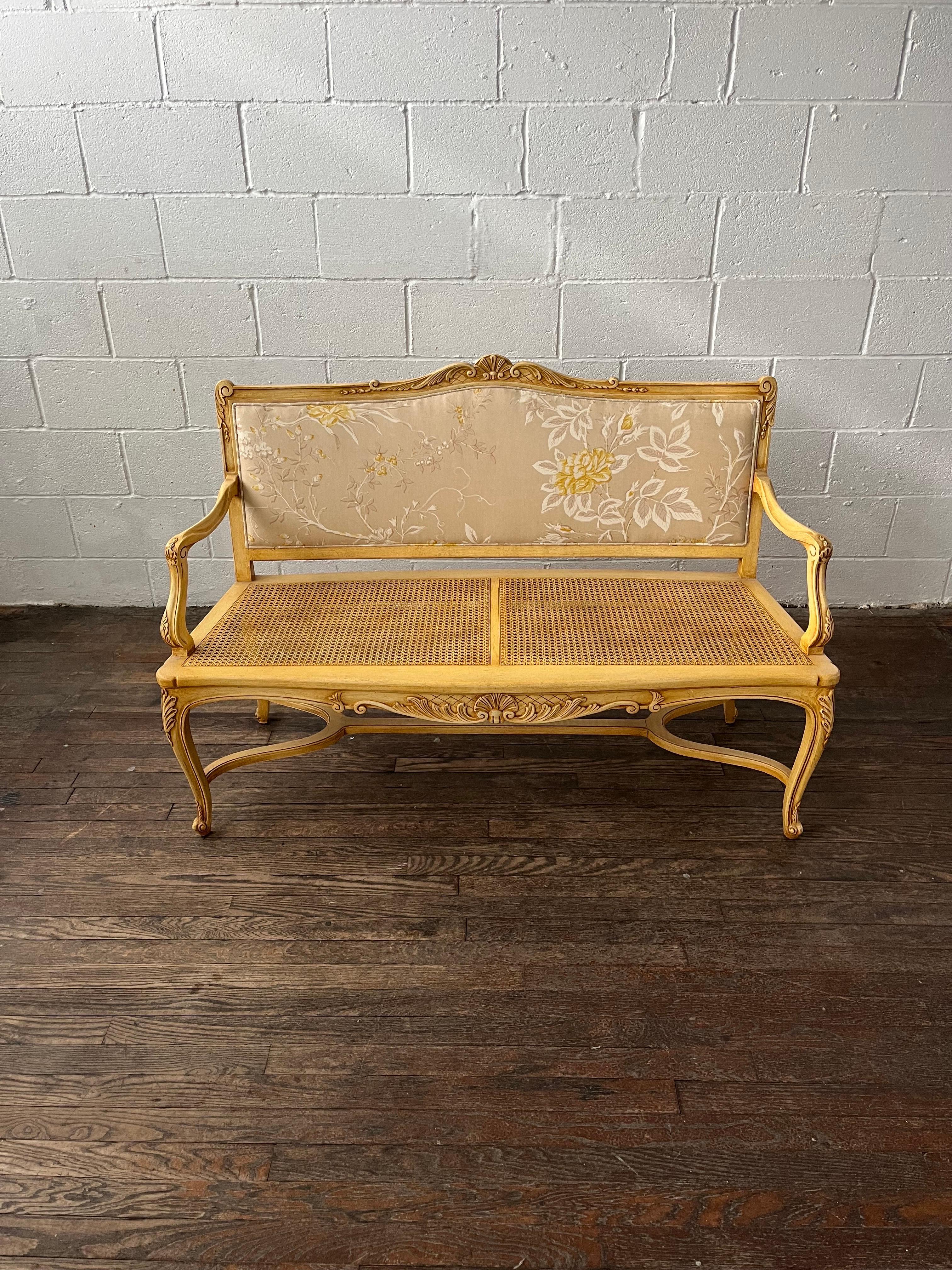 Beautifully appointed settee in a provincial style. Intact cane bench seat with upholstered pillow cushion with matching upholstered back rest. Nicely detailed scrolling on frame. 
Curbside to NYC/Philly $350