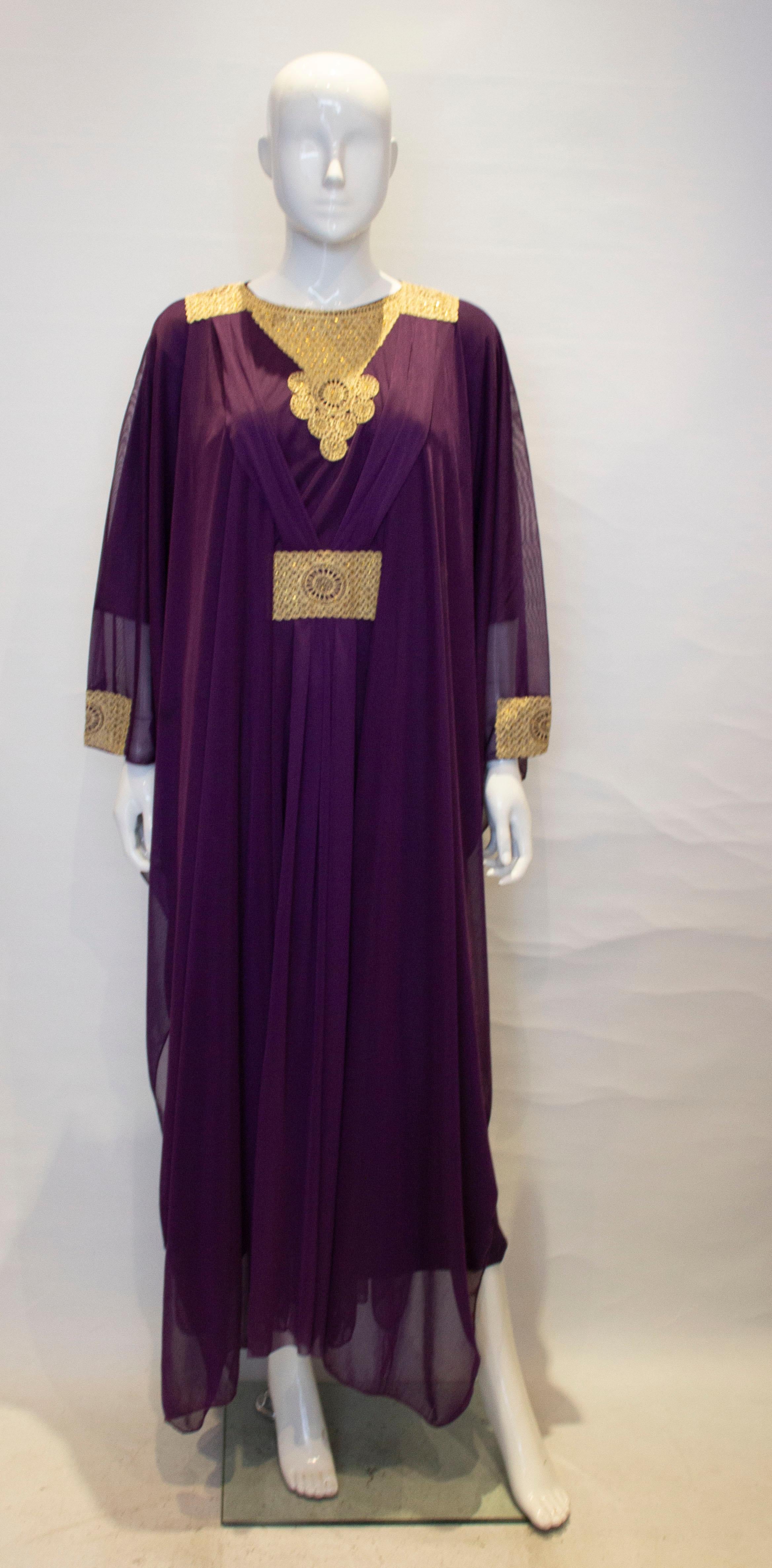 A headturning vintage purple and gold kaftan. The kaftan has two layers, and inner column and the outer flowing kaftan. It has gold trim on the front , back and cuffs, and pleats on the shoulder. 