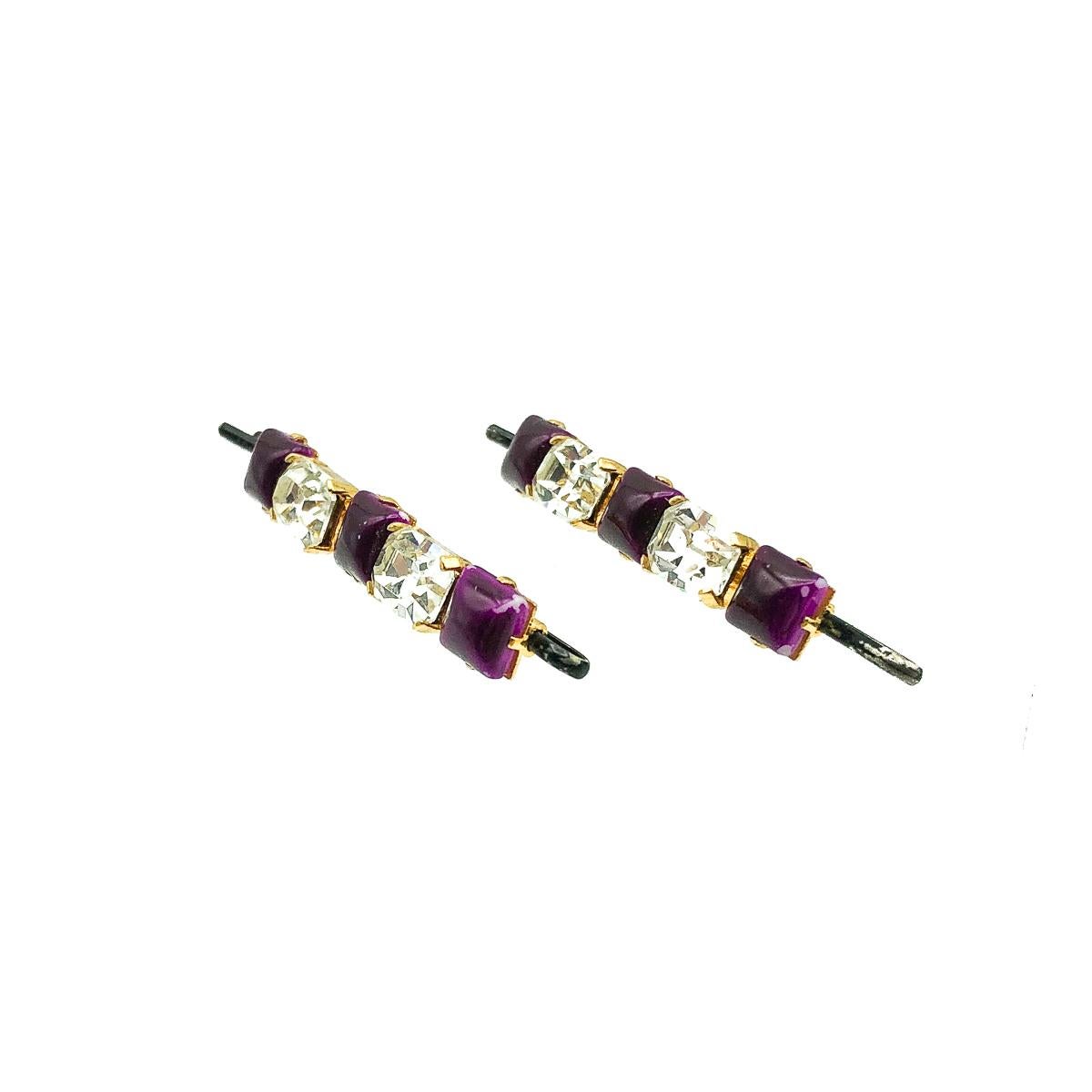 A pair of Vintage Crystal Hair Slides. Featuring a five stone row of claw set, emerald cut crystals which sparkle adorably alongside painted purple glass squares. Crafted in rich gold plated metal with a traditional hair grip attached through a long