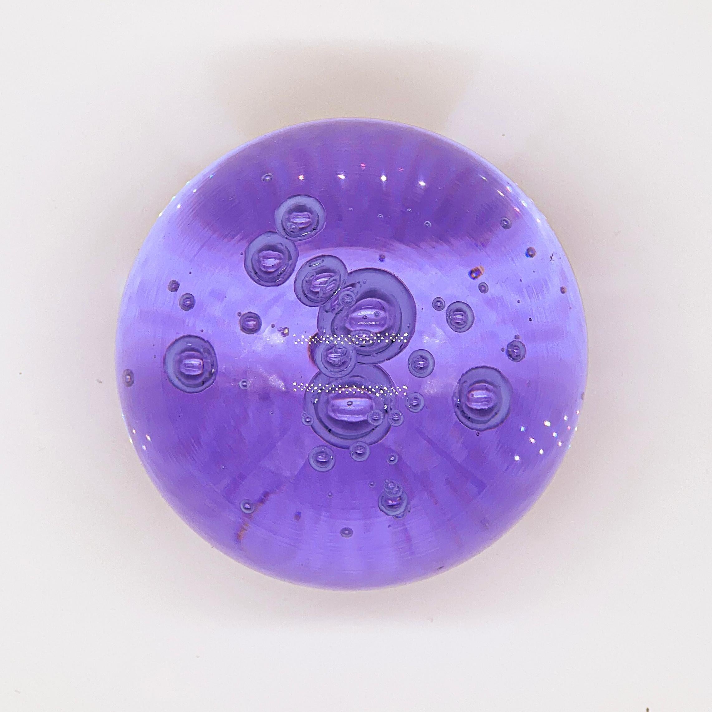 Presse-papier Vintage Murano en forme de sphère avec un fond plat pour le faire tenir debout. Réalisé dans un verre violet profond et vibrant, il présente des bulles incluses qui lui confèrent profondeur et volume. C'est un objet très attrayant qui