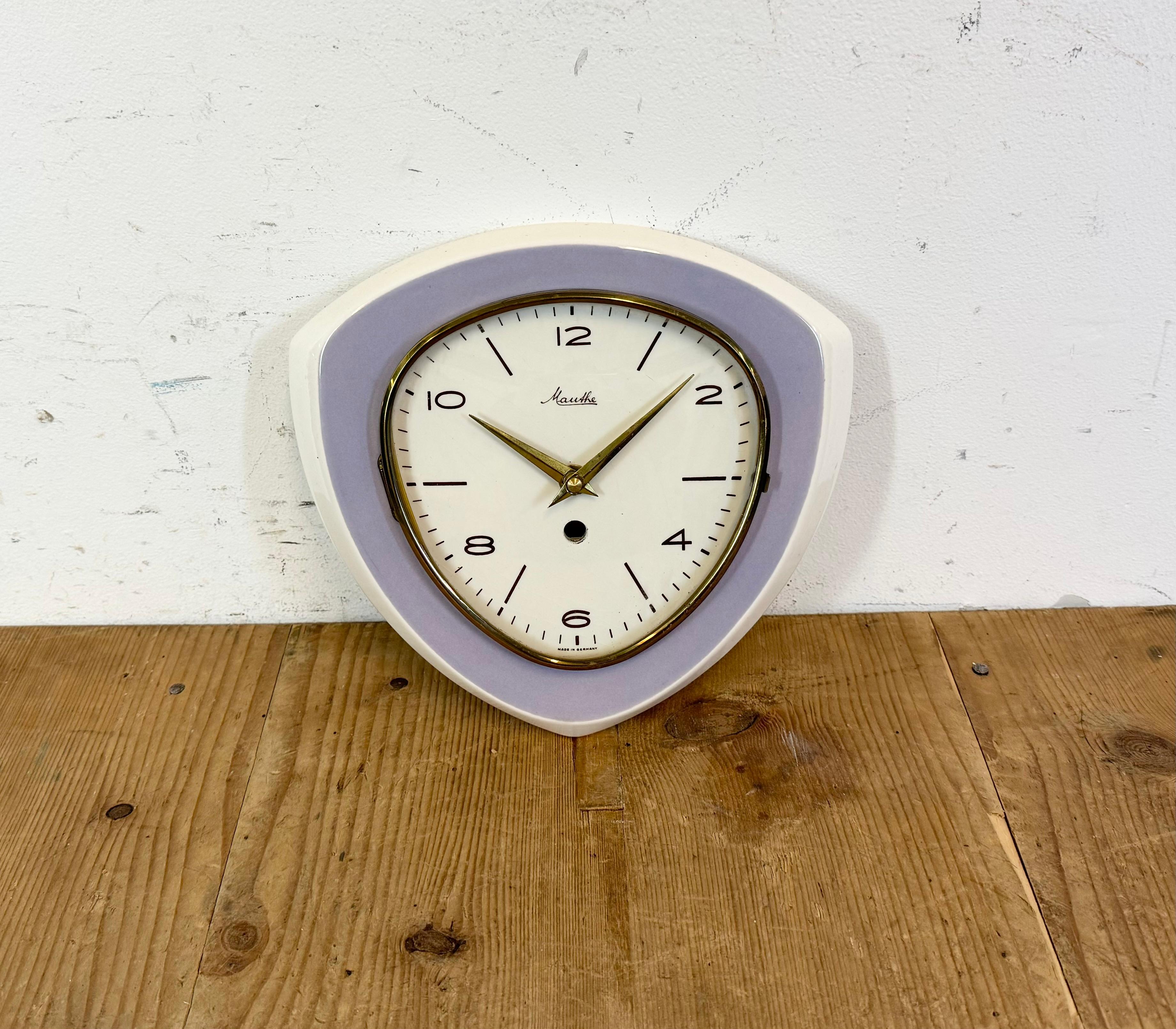Vintage triangle wall clock was made by Mauthe in Germany during the 1970s .. It features a white and purple porcelain body and a convex clear glass cover with brass ring. The former winding clock has been converted into a battery-powered clockwork