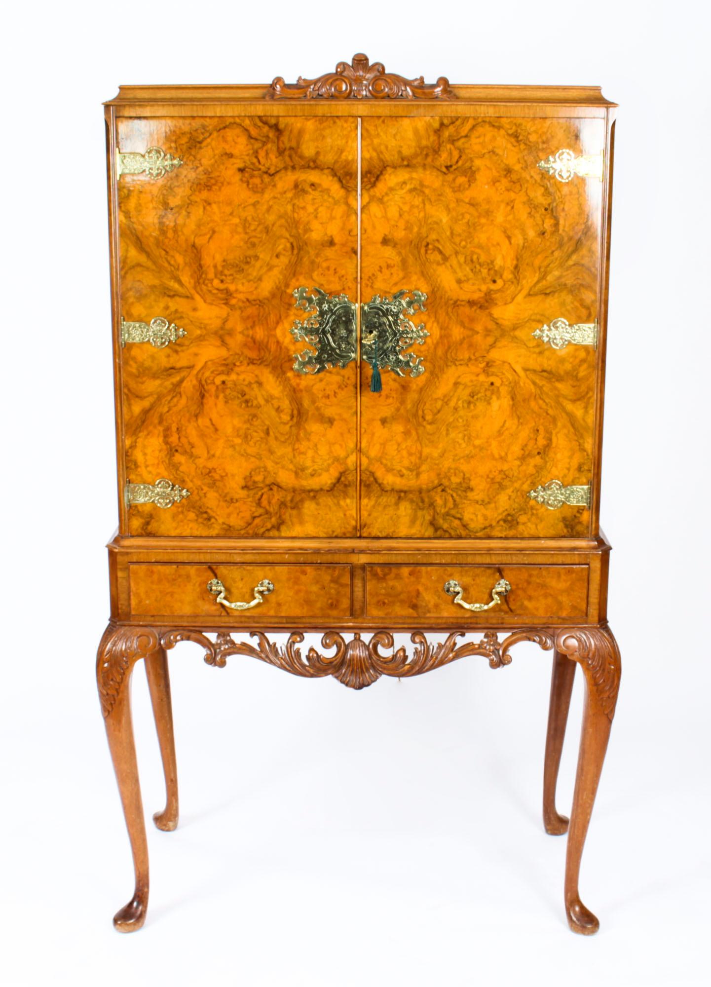 This is a fantastic vintage Queen Anne Revival burr walnut cocktail cabinet with wonderful hand carved decoration dating from the mid-20th century.

The doors open to reveal a stunning fitted maple fitted interior with mirrored back, a glass shelf